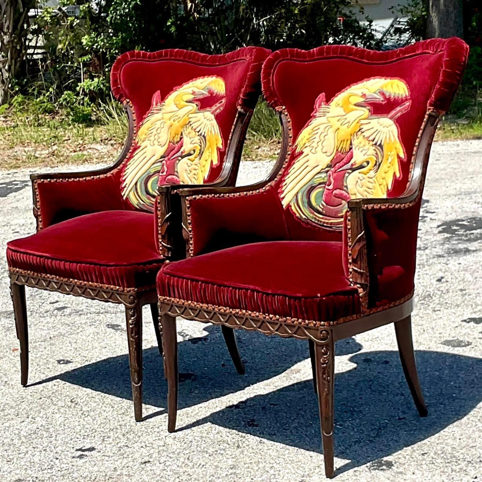 An extraordinary pair of vintage velvet arm chairs. A deep red velvet with a ruched detail along the edge. A fabulous crane design on the back of each chair back. Hand carved detail on the wood trim. Acquired from a Palm Beach estate.