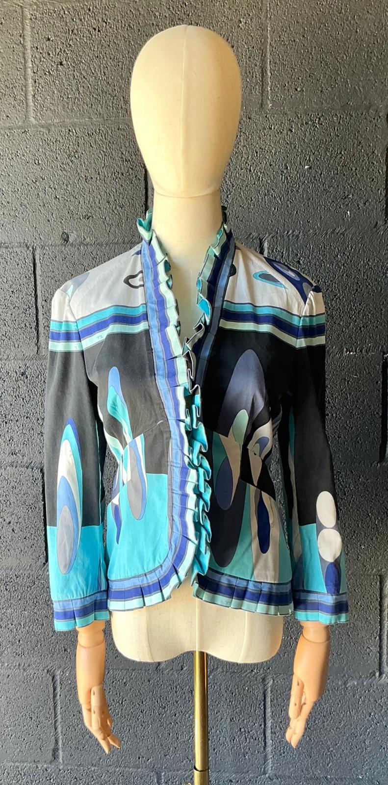 Eleva il tuo guardaroba con questa splendida blusa con volant Emilio Pucci in stile Vintage Boho, una fusione da sogno tra l'iconica arte di Emilio Pucci e il suo stile bohémien senza sforzo. Realizzata in un tessuto leggero e fluente, la blusa