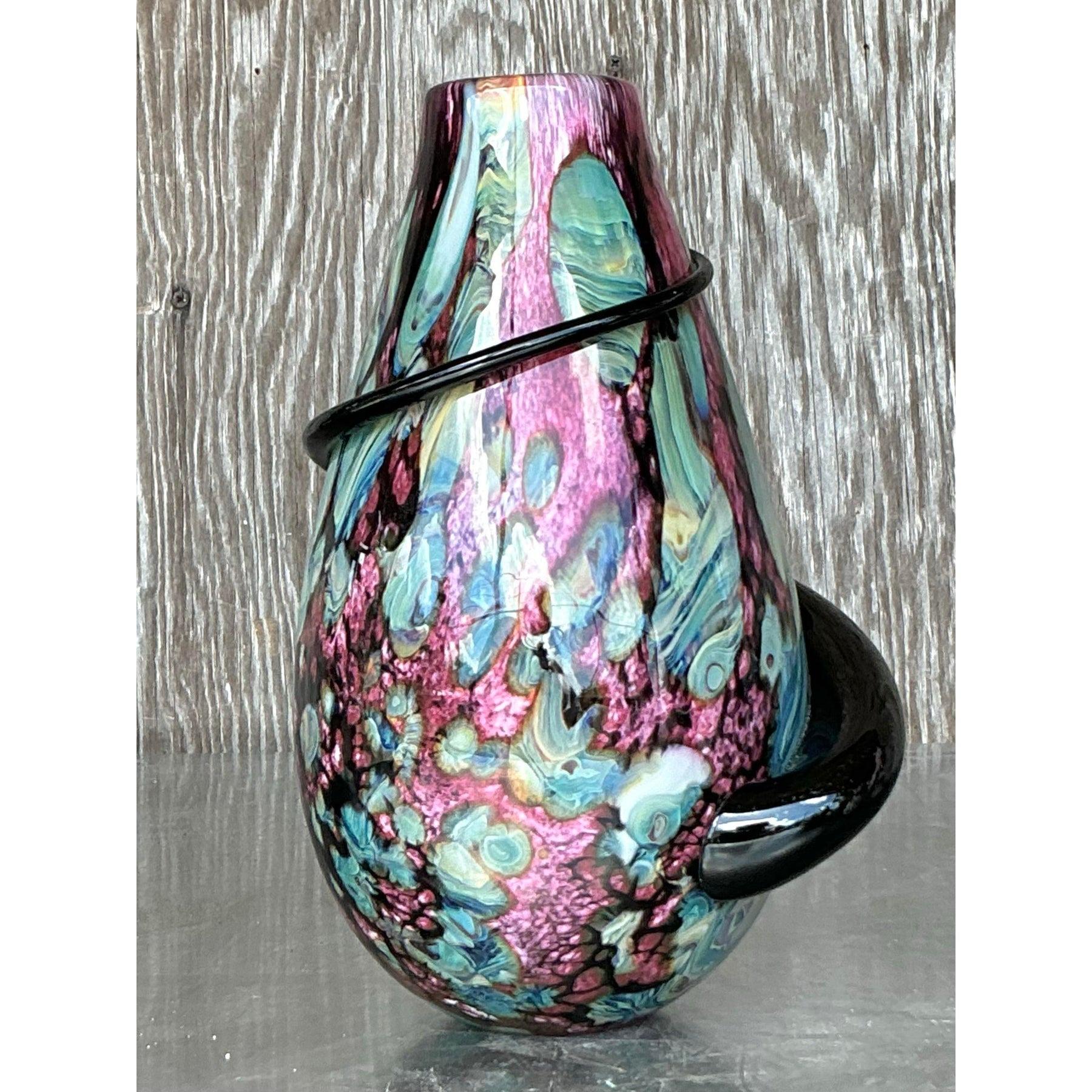 Ce vase exquis en verre d'art soufflé à la main est une fusion captivante de couleurs et de formes. Le motif marbré saisissant, qui présente des tourbillons de rose, de bleu et de crème, est complété par un ruban de verre noir audacieux et