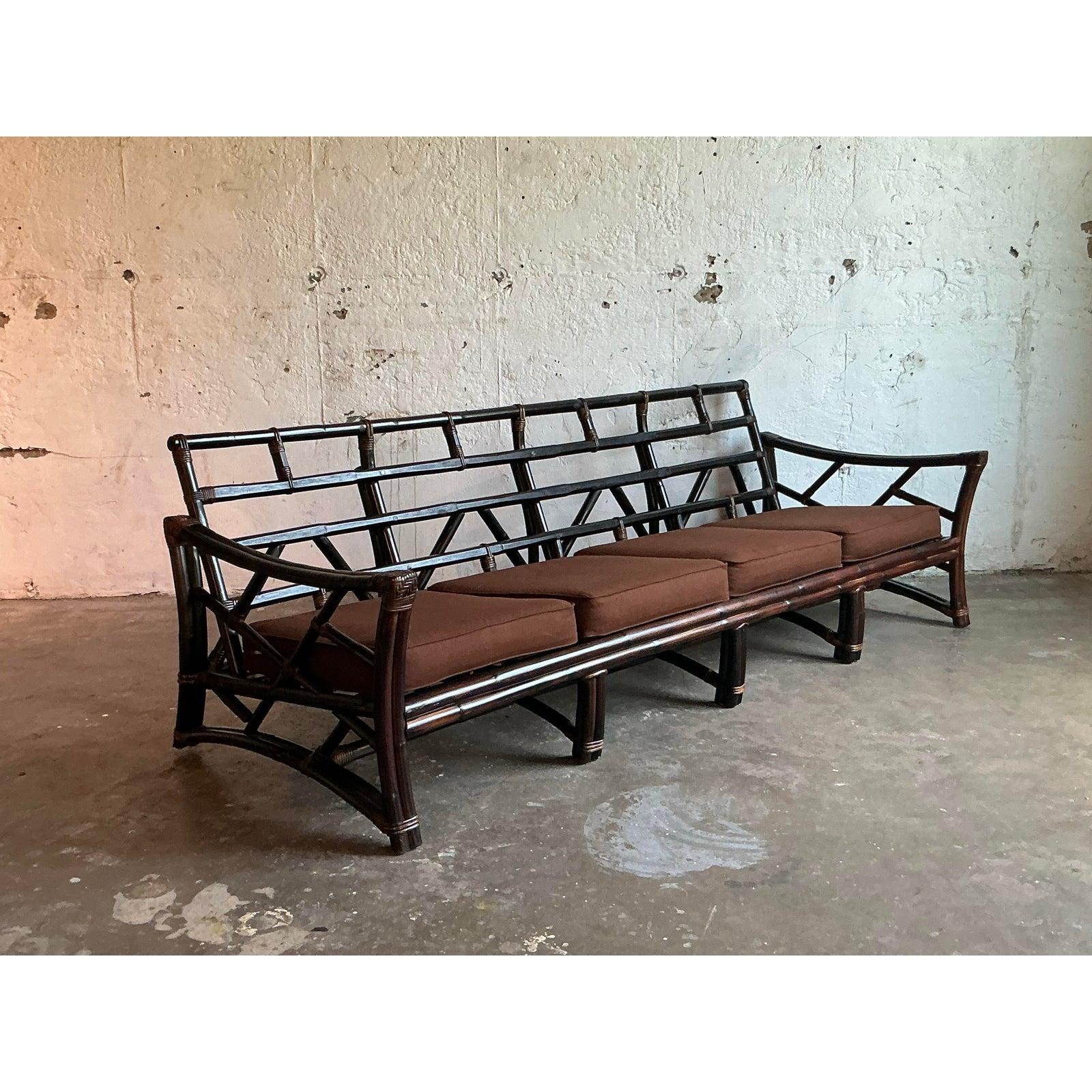 Adopta la elegancia atemporal del diseño moderno tropical con este excepcional sofá vintage de brazos inclinados. Fabricada a la manera icónica de Ficks Reed, esta pieza presenta una robusta estructura de ratán con un espectacular acabado ebonizado,