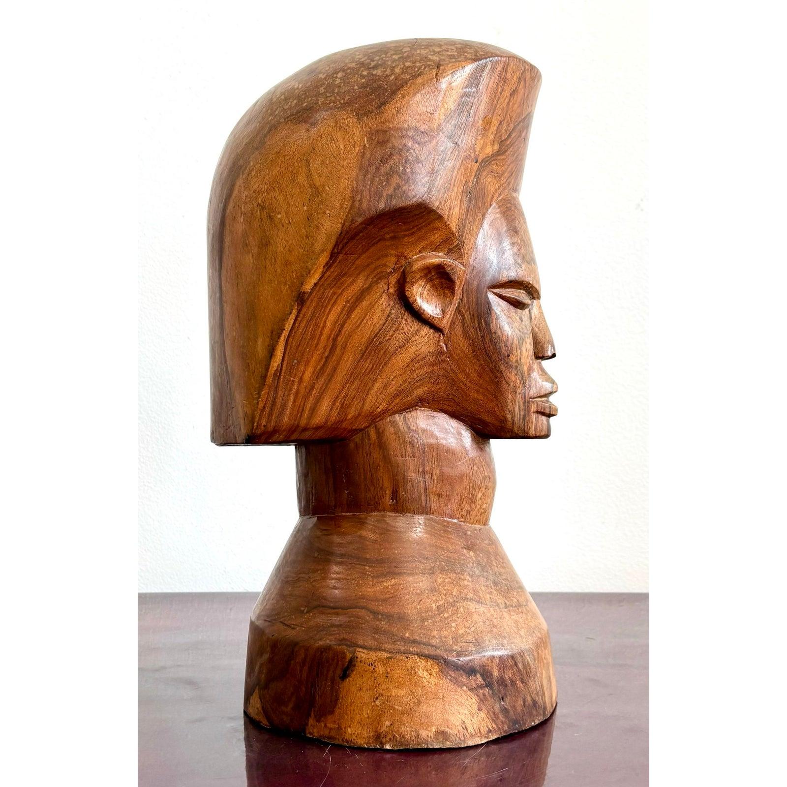 Questo busto in legno intagliato emana una forza tranquilla e una presenza senza tempo. Scolpita in un legno ricco di venature, la figura dal collo allungato, gli zigomi alti e gli occhi chiusi suggeriscono una calma introspezione. I tratti lisci e