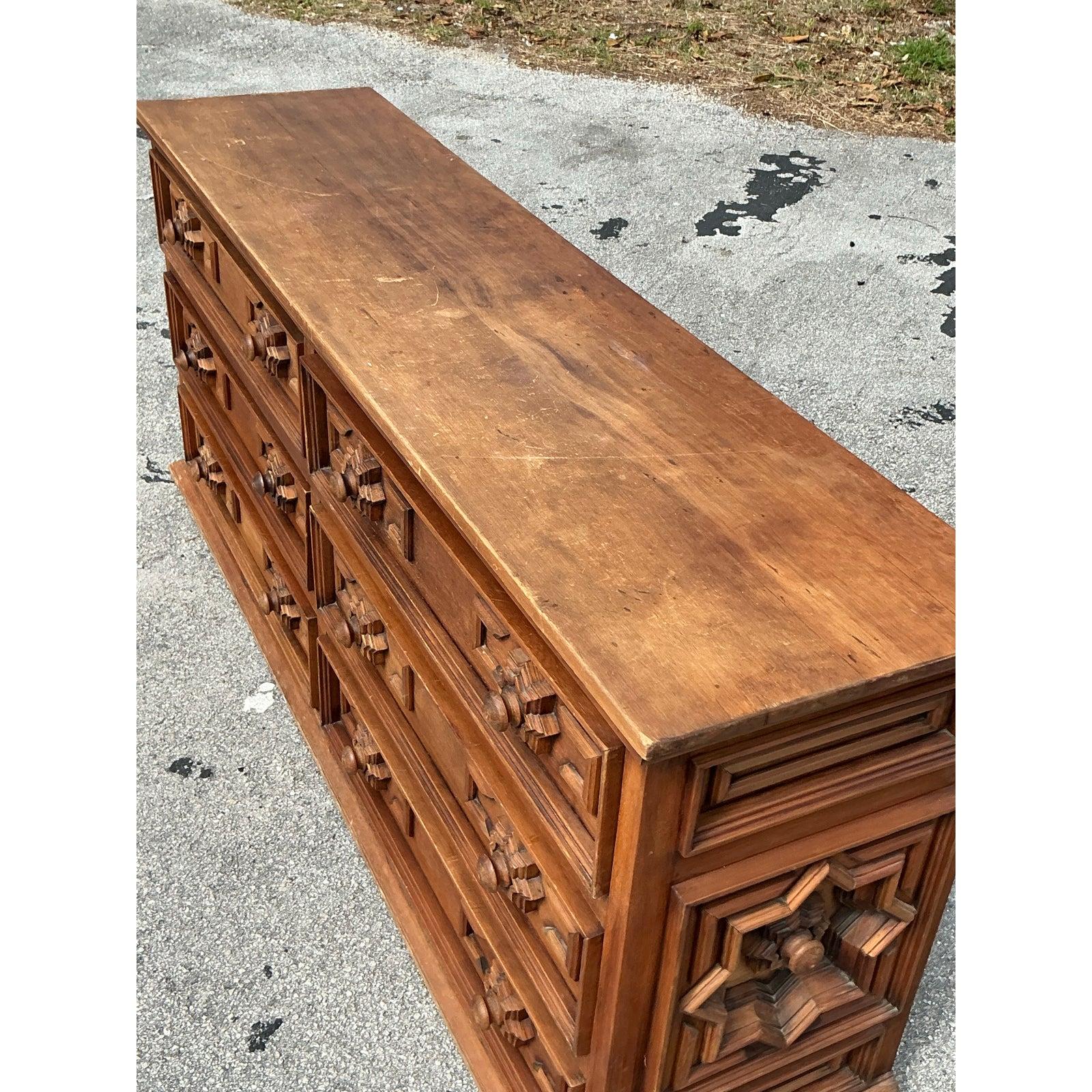 Aggiungi un carattere deciso e un'anima vintage al tuo spazio con questo comò a sei cassetti di ispirazione Boho, caratterizzato da intricati motivi a stella intagliati e da una robusta lavorazione del legno. La ricca patina e la ferramenta