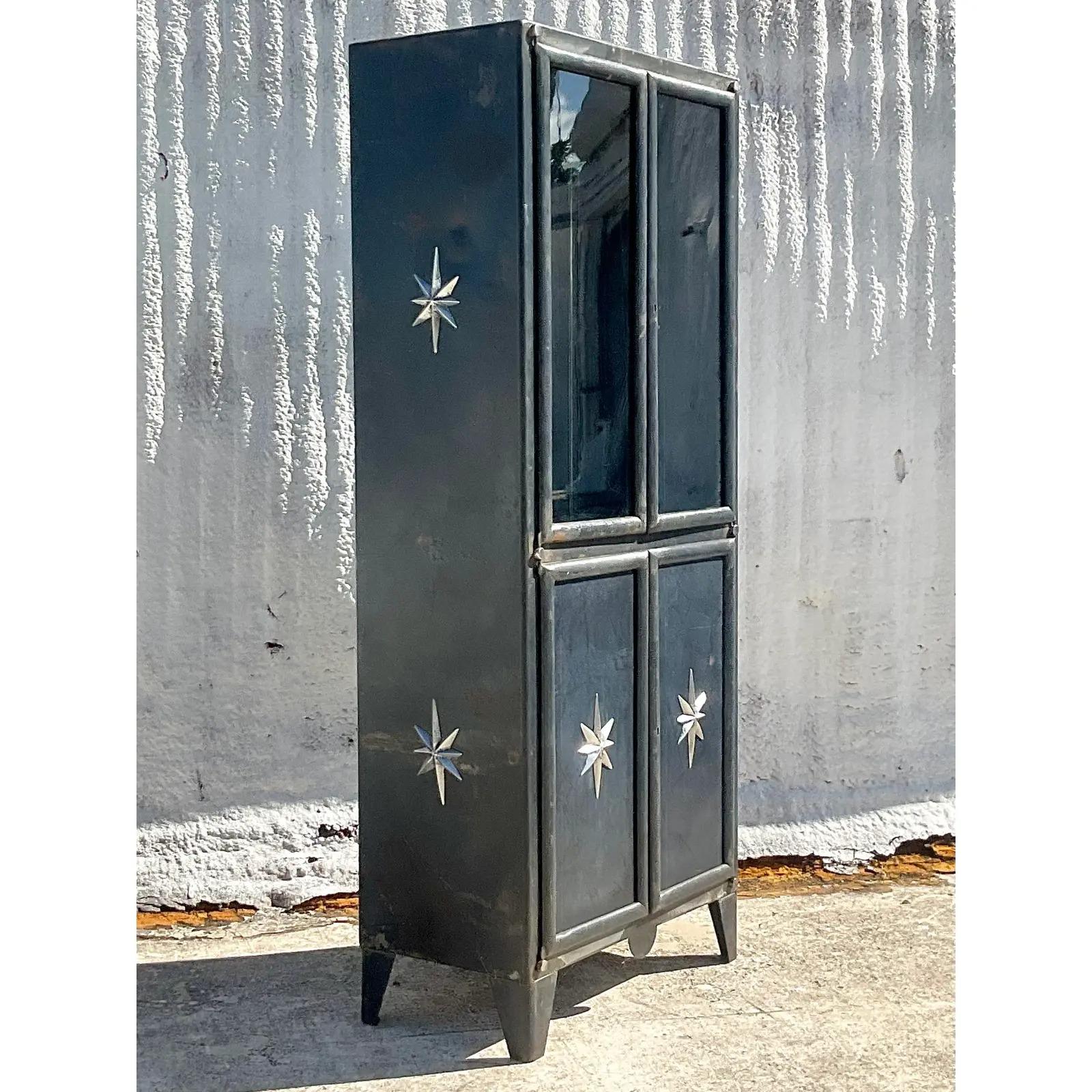 A fantastic vintage Boho metal storage cabinet. Fabulous silver stars adorn this black steel cabinet. Two separate sections with two glass shelves above and one below. Acquired from a Palm Beach estate.