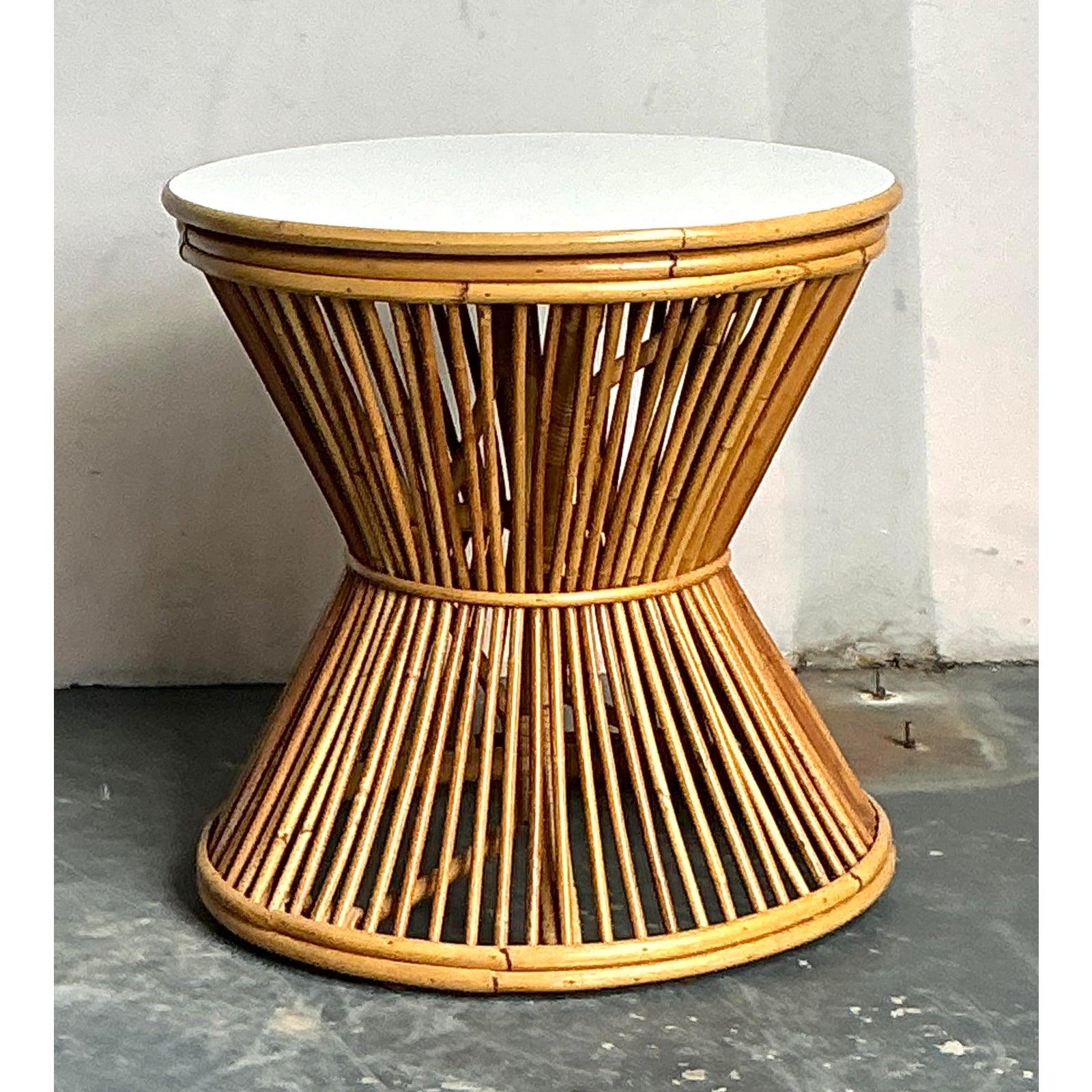 This charming vintage side table embodies the relaxed elegance of Mid-Century Coastal design, utilizing thin rattan sticks to create a striking hourglass silhouette. The open, airy construction forms a visually dynamic pedestal base, expertly