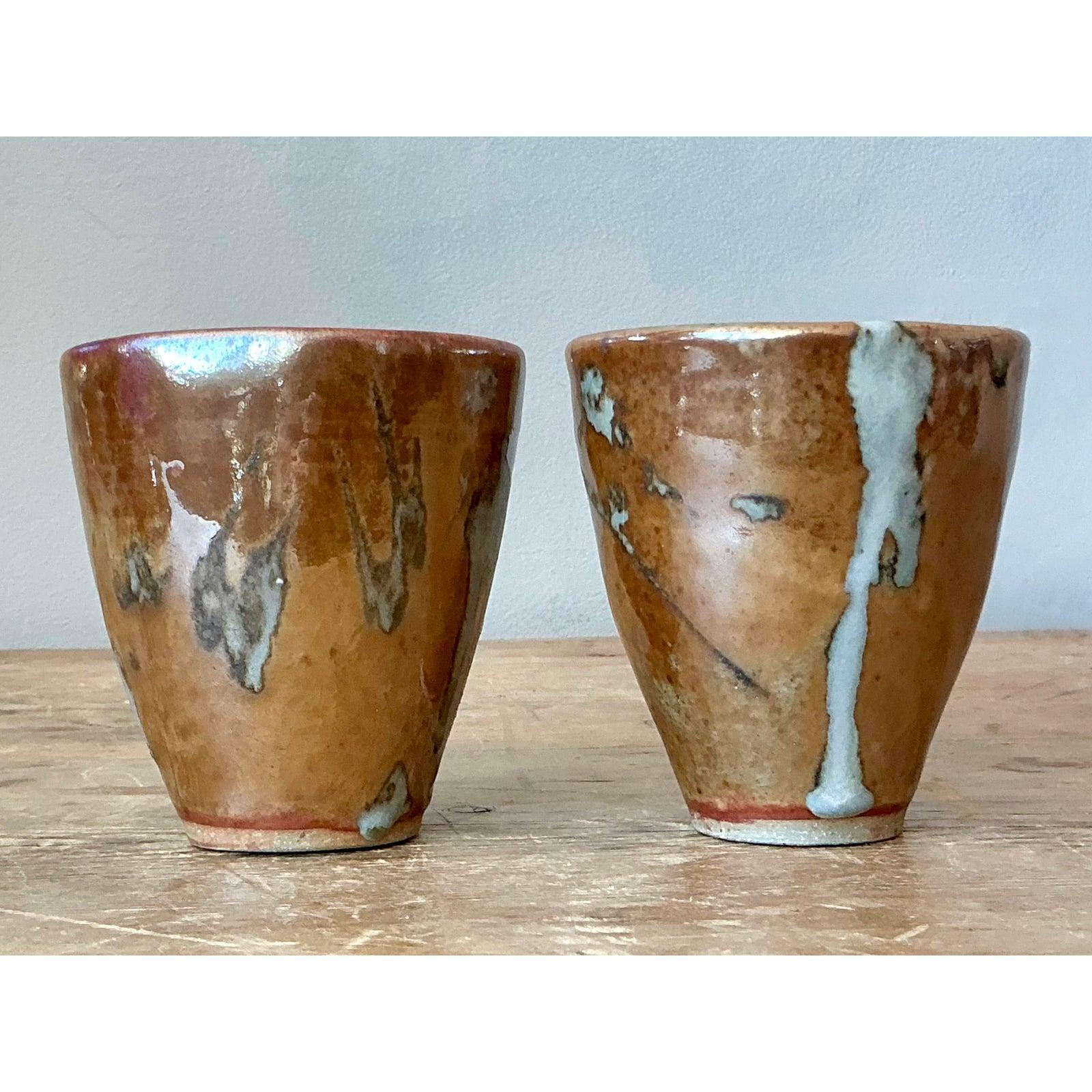 This exquisite pair of studio pottery cups showcases masterful glazing techniques, drawing inspiration from Japanese rustic ceramics and Mid-Century American craft. Hand-thrown into an elegant conical shape, the cups are finished in a rich, glossy