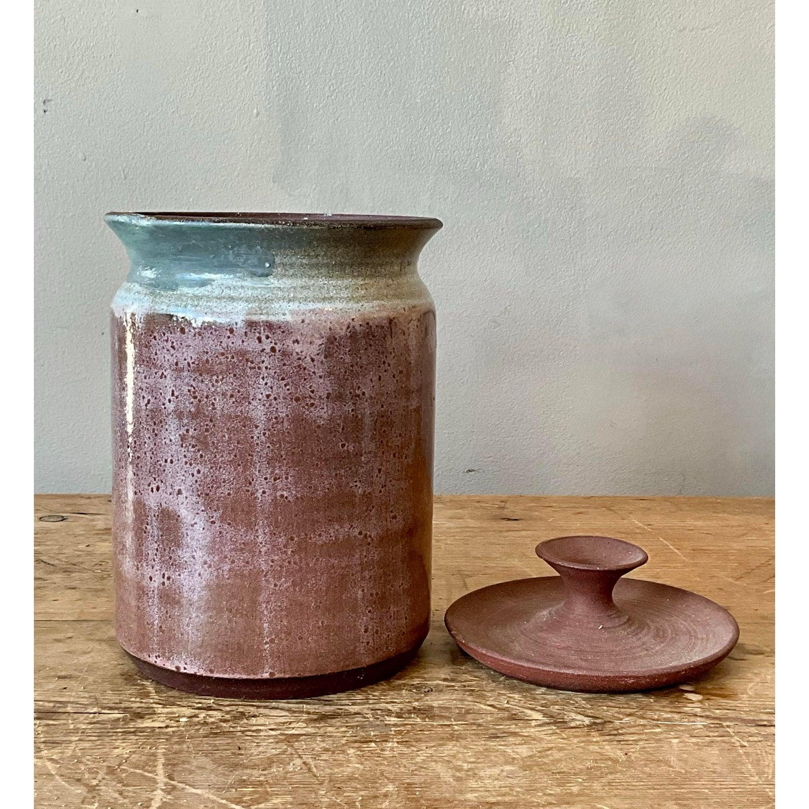 Questo caratteristico vaso con coperchio è una testimonianza degli smalti dinamici e della bellezza tattile delle ceramiche da studio del Mid-Century. Realizzato a mano, il corpo cilindrico in gres è caratterizzato da una complessa applicazione di