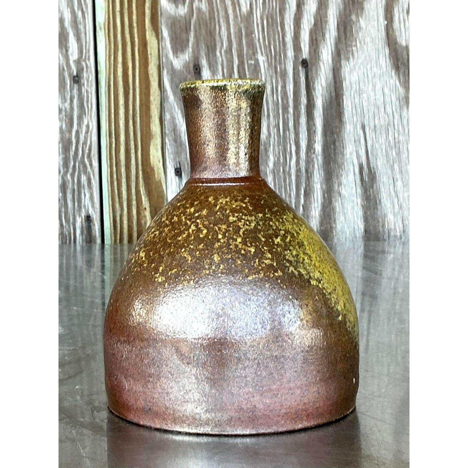 Embrace the subtle beauty of handcrafted ceramics with this charming vintage studio pottery piece, reminiscent of a traditional sake bottle or a refined bud vase. Its classic form, featuring a gently rounded body tapering to an elegant cylindrical