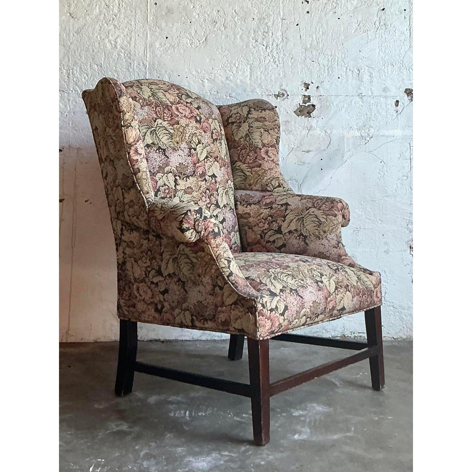 Embrassez le charme romantique du design de la campagne anglaise avec ce fauteuil à oreilles vintage exquis. Enveloppée d'une tapisserie florale luxuriante de haute qualité, cette chaise est une célébration de la forme classique et de la beauté