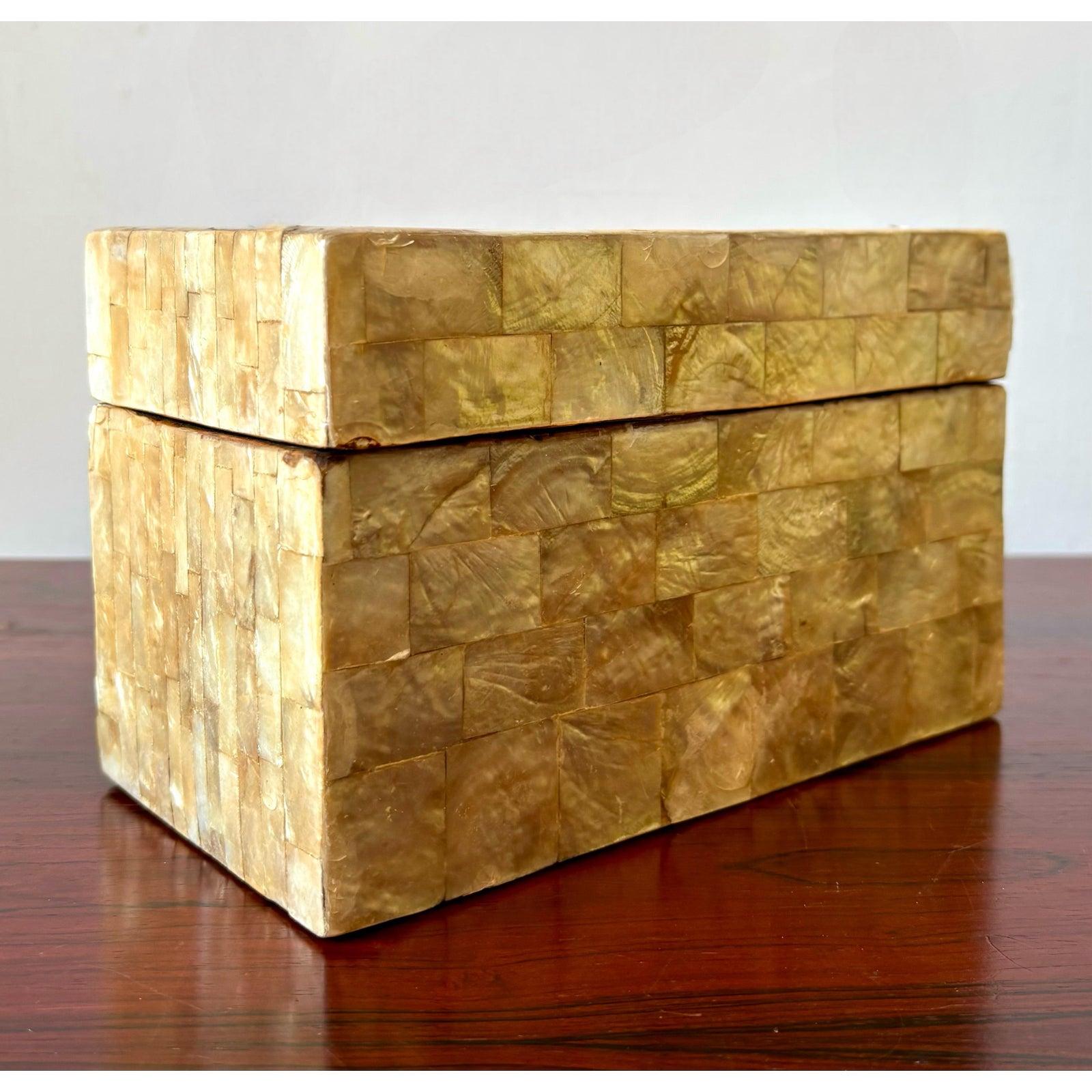 Questa elegante scatola decorativa presenta un esterno a mosaico lucido composto da tessere quadrate di varie tonalità di beige caldo e traslucido e avorio dorato, che ricordano le conchiglie di capiz o il corno lucidato. Il coperchio, mostrato