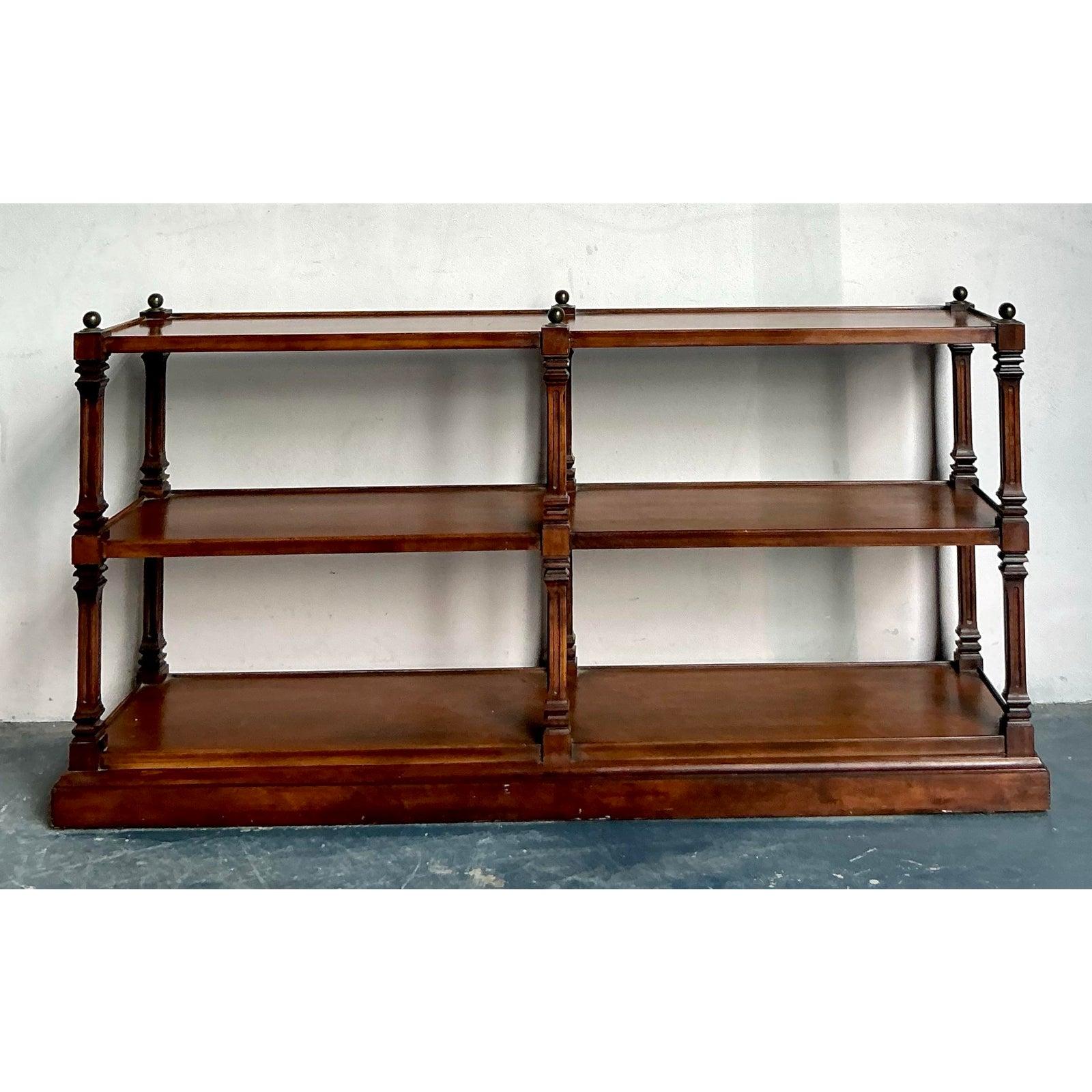 This distinguished low etagere or console table embodies the refined symmetry and classical detailing of Regency design, offering a versatile piece of display furniture. Constructed from a deep mahogany-toned wood with a high-gloss finish, the unit