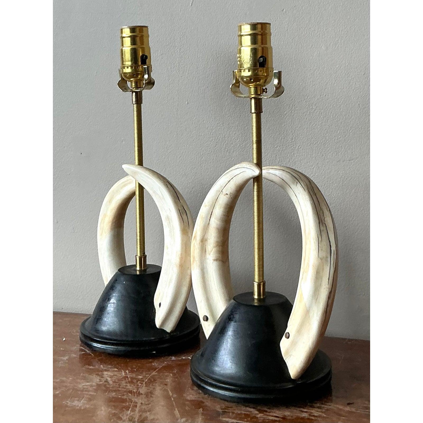 Uncommon and highly stylized, this pair of Vintage Boho Chic Tusk Table Lamps offers an exotic touch to any discerning interior. Each lamp features elegantly curved, faux tusk-like forms that encircle a central brass rod, all anchored by a striking