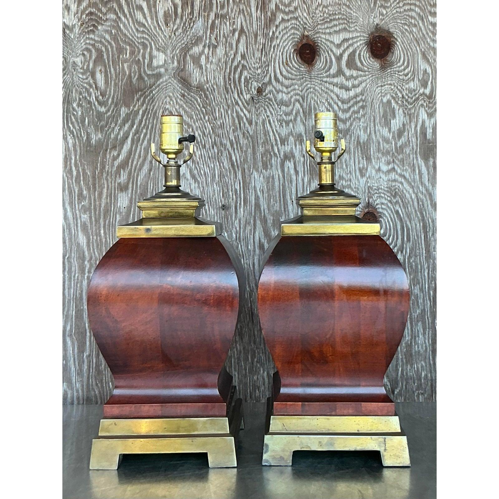 This striking pair of vintage wood and brass lamps blends timeless elegance with bold, sculptural form. Crafted with a gracefully curved wood body in a rich, reddish-brown tone and mounted on tiered brass bases, these lamps exude refined bohemian