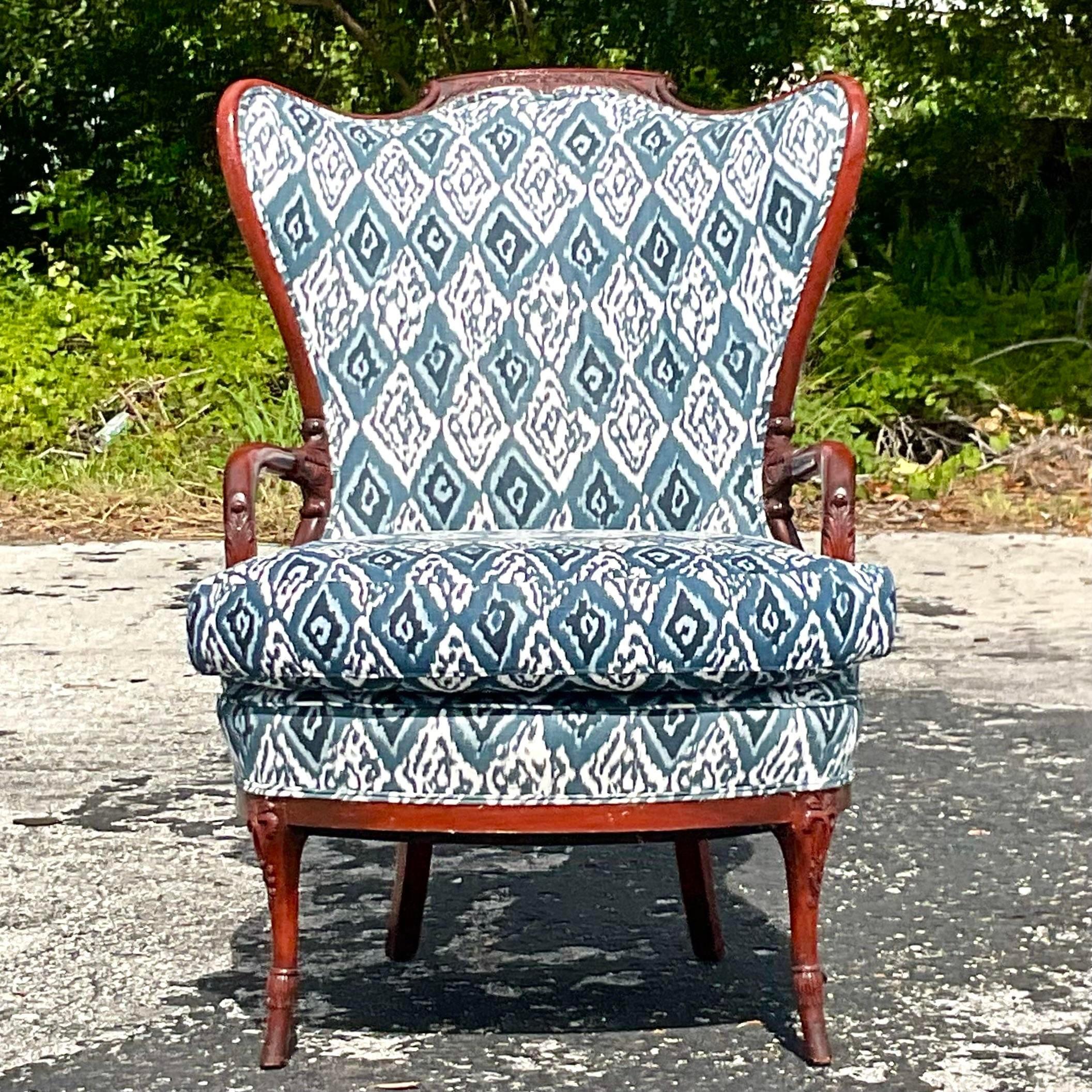 A fantastic vintage Boho wingback chair. A chic Schumacher Ikat print in beautiful shades of blue. Hand carved wood carved detail. Acquired from a Palm Beach estate.