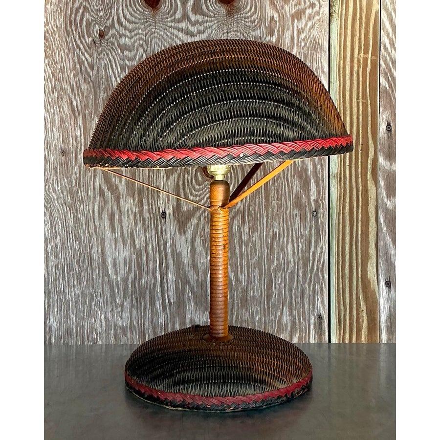 Add a touch of bohemian charm to your living space with this vintage woven rattan table lamp. Featuring an intricately handwoven design with a dome-shaped shade, this lamp showcases natural textures enhanced by subtle red and black braided accents.