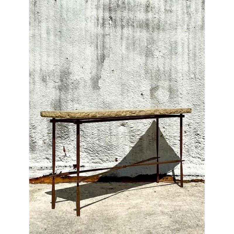 Discover the compelling blend of natural texture and robust form with this vintage console table, featuring a substantial limestone top resting upon a wrought iron base. The earthy, tactile surface of the limestone contrasts beautifully with the