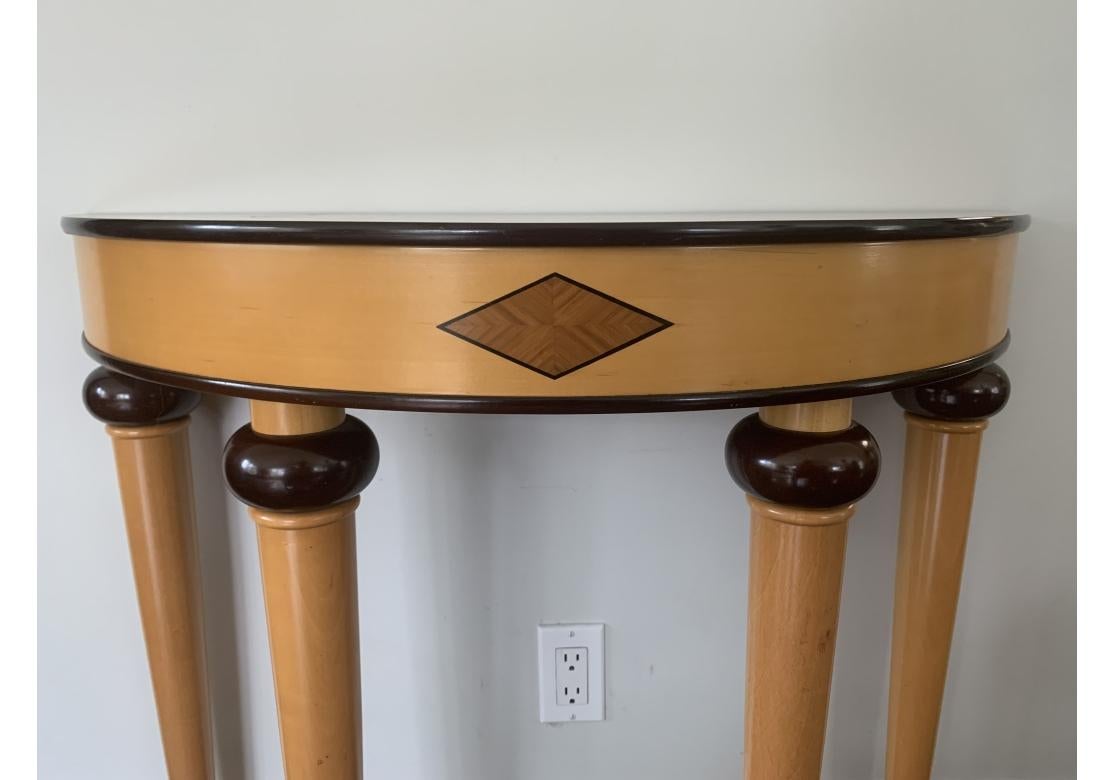 Ein Demi-Lune-Tisch im Art-déco-Stil mit Mahagoni-Verzierungen, die den Fries mit einem eingelegten Rautenmotiv flankieren. Der Tisch ruht auf zylindrischen, sich verjüngenden Beinen mit einem Mahagoni-Element in Duttform. Gekennzeichnet wie
