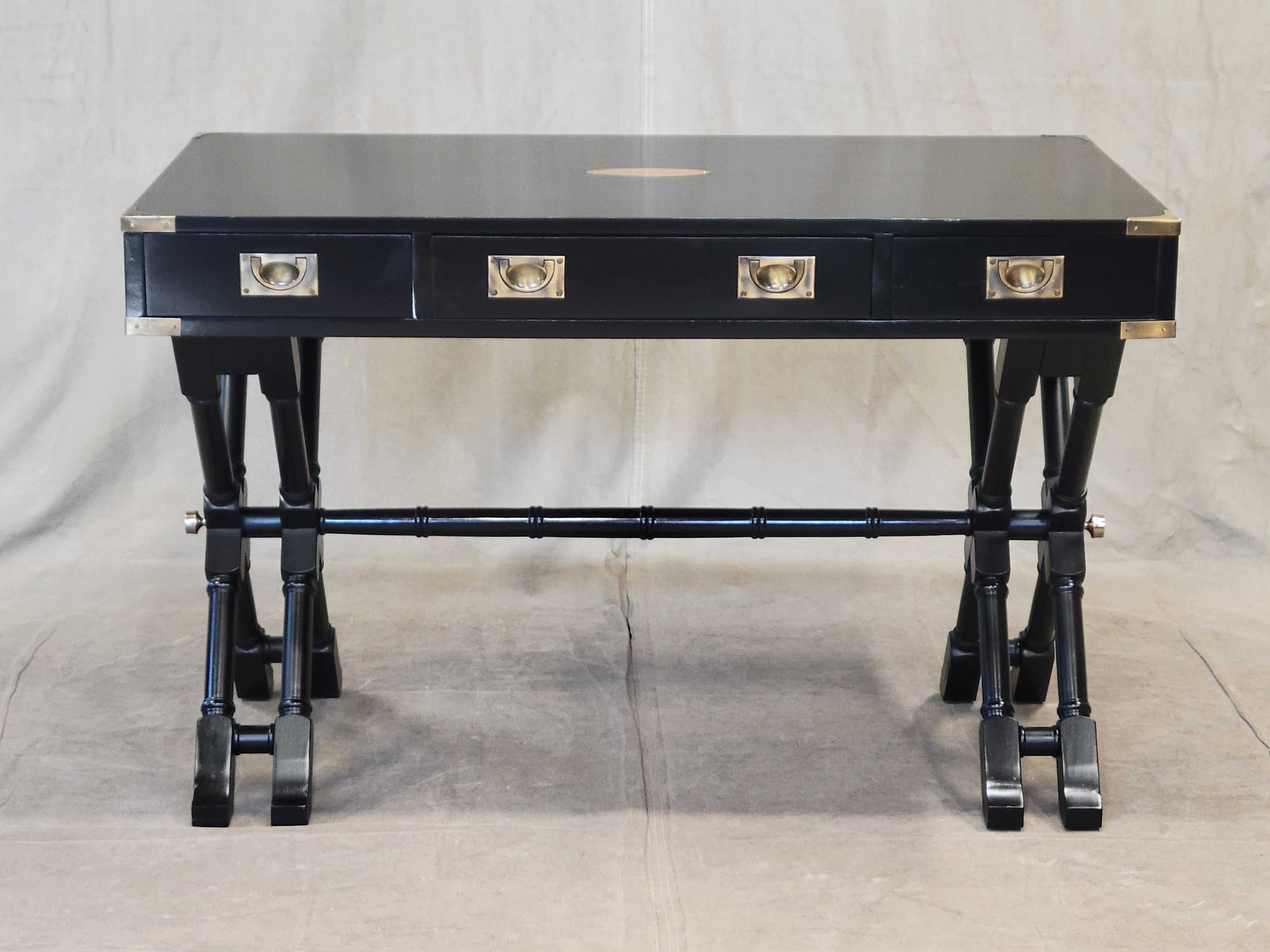 This stunning vintage Bombay Company campaign style writing desk sits on a beautifully carved faux bamboo base. It has been professionally refinished with stunning black lacquer. Original campaign style brass hardware accents contrast beautifully