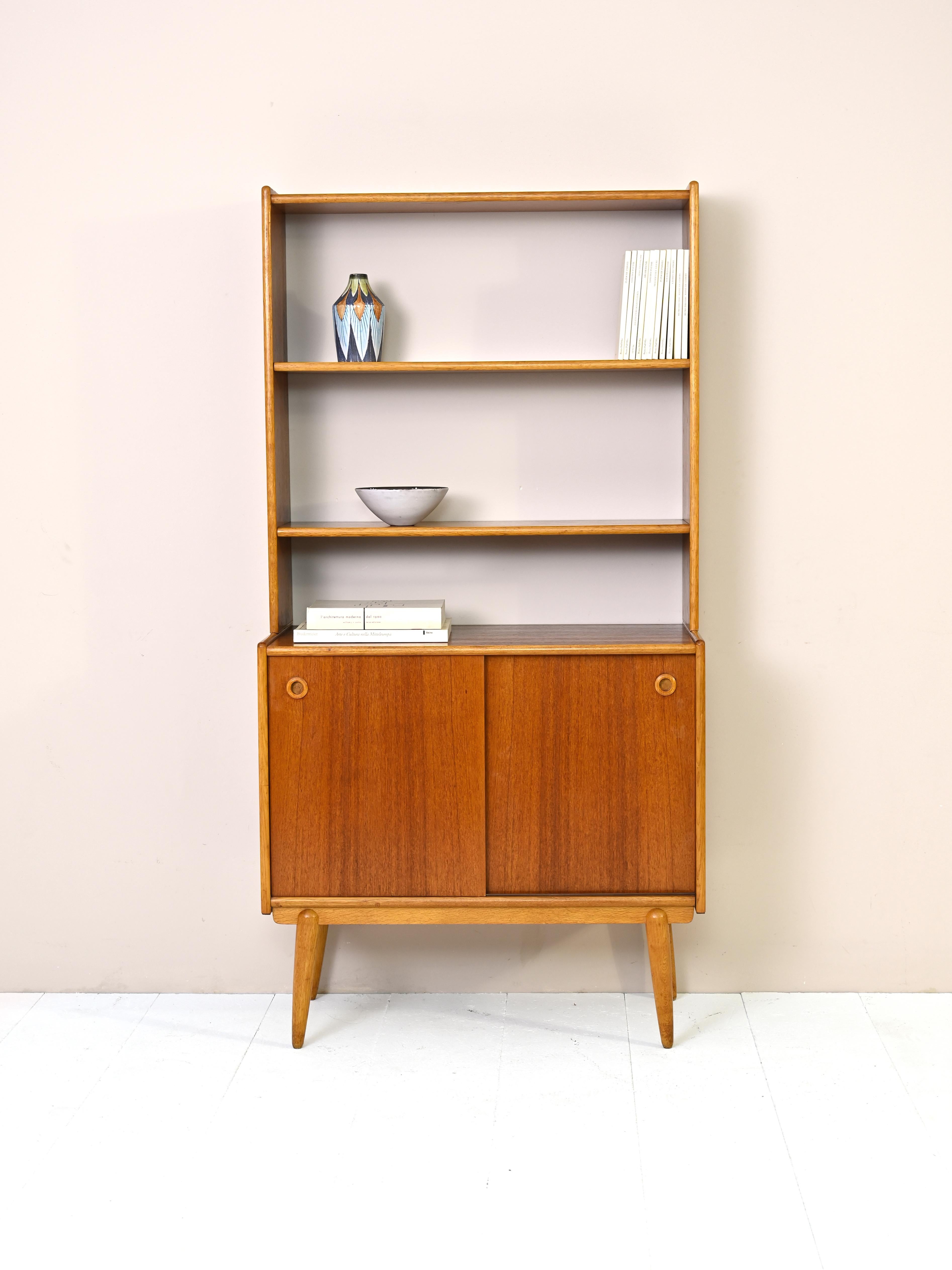 Original vintage teak furniture from Scandinavia, consisting of two parts. The upper part is a bookcase equipped with adjustable height shelves, the lower part is a cabinet with sliding doors.
An elegant and functional piece of furniture that can