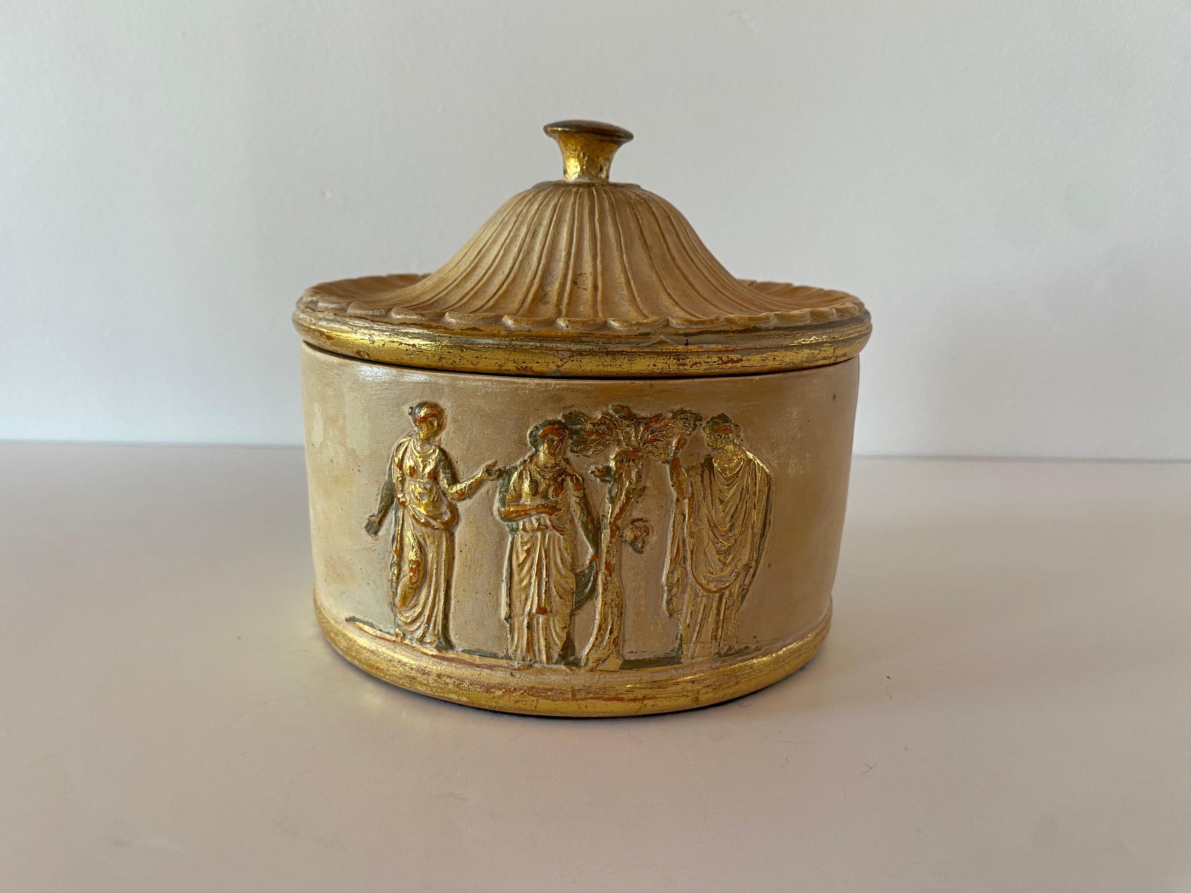 Bellissima scatola vintage in gesso ceramico realizzata in Italia. Incredibilmente scolpito in stile neoclassico, il pezzo è caratterizzato da  immagini elleniche di sacerdotesse e nobili in oro. L'interno della scatola è colorato in una tonalità di