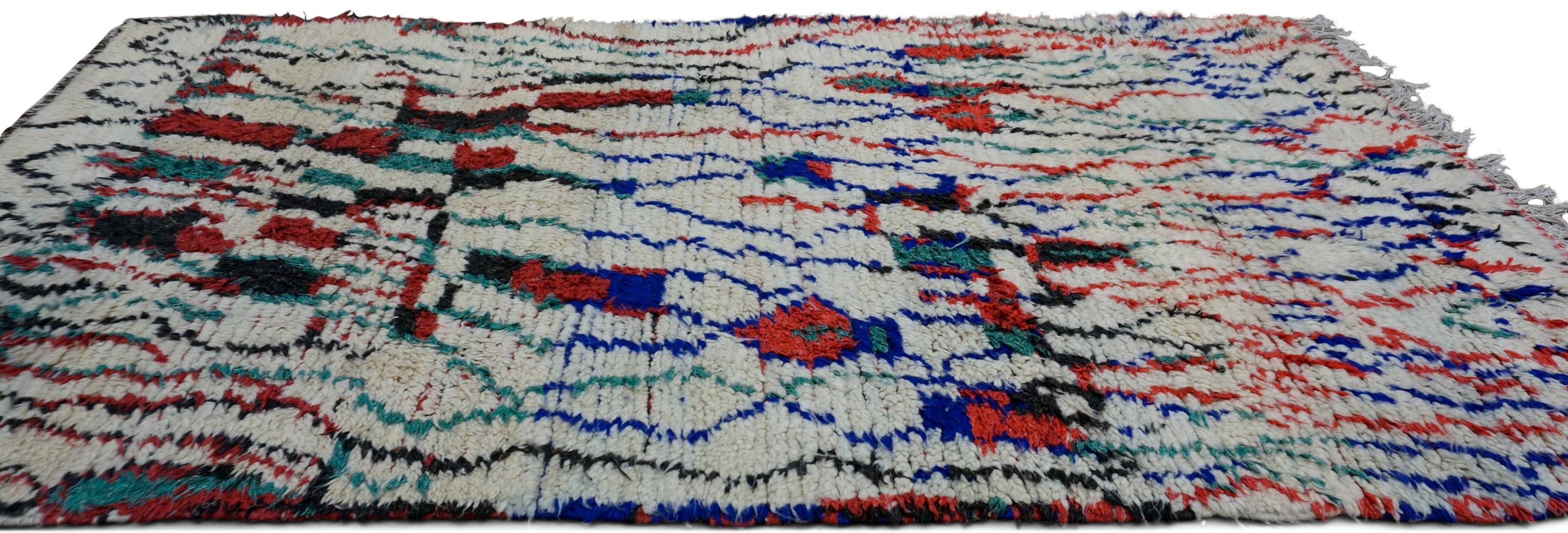 Dieser handgeknüpfte Wollteppich ist ein fesselndes Beispiel für die Boucherouite-Tradition, bei der Kreativität und Spontaneität im Vordergrund stehen. Der Teppich zeichnet sich durch seine kühne Farbpalette und seine abstrakte Freiformkomposition