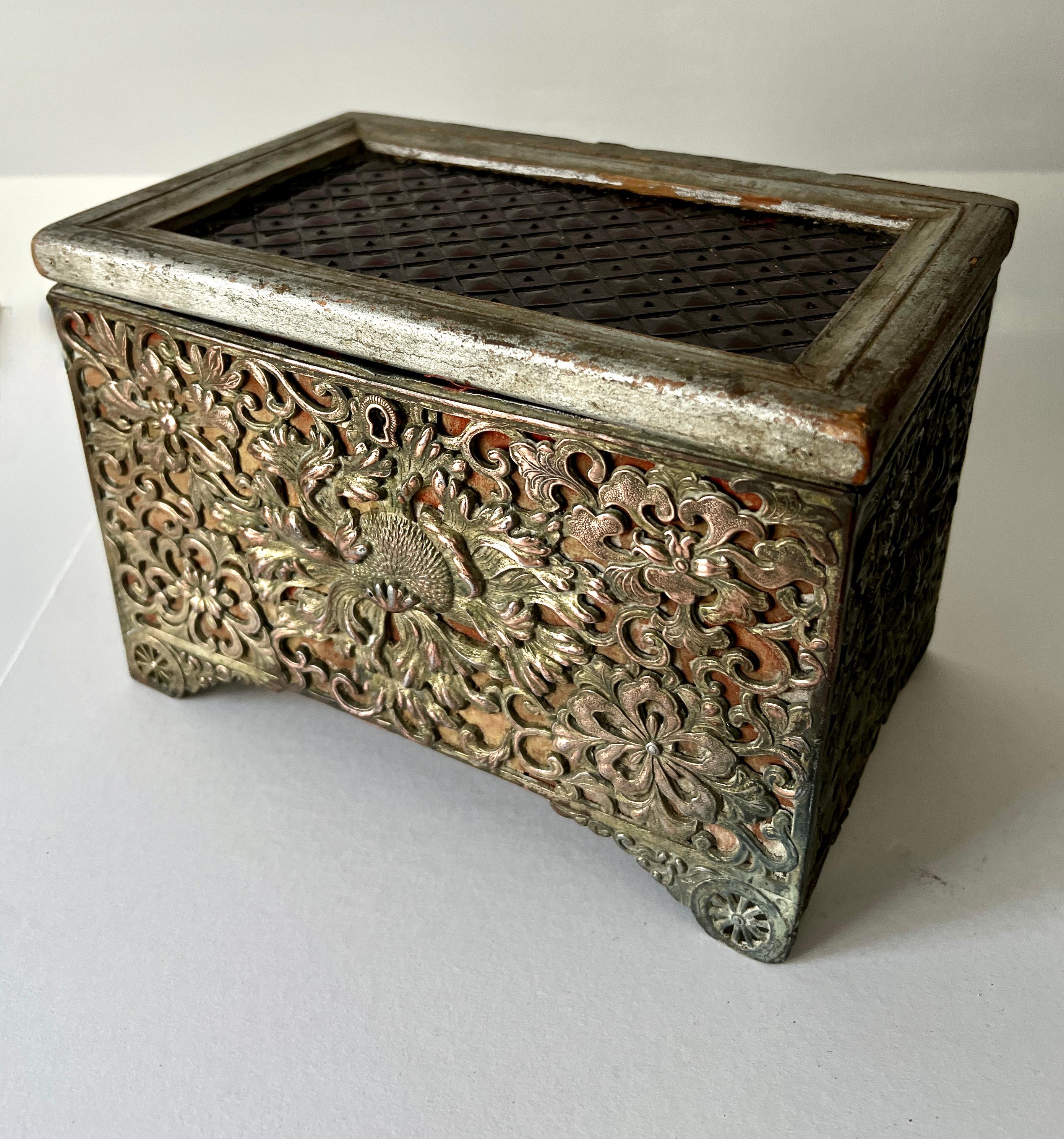 Un cofanetto in legno vintage unico nel suo genere, splendidamente lavorato a mano e impreziosito da un esterno in argento repoussé. Il coperchio, realizzato in legno con foglie d'argento, presenta un sorprendente inserto in vetro artistico che