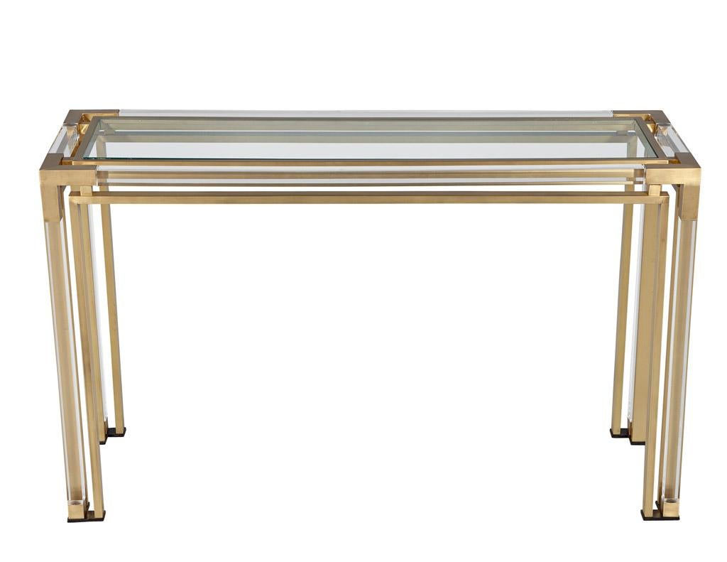 This unique vintage console table brings together modern styling and timeless French craftsmanship. Circa 1970's, this console table features a simple yet elegant design with a glass top, acrylic accents, and brass frame. The combination of these