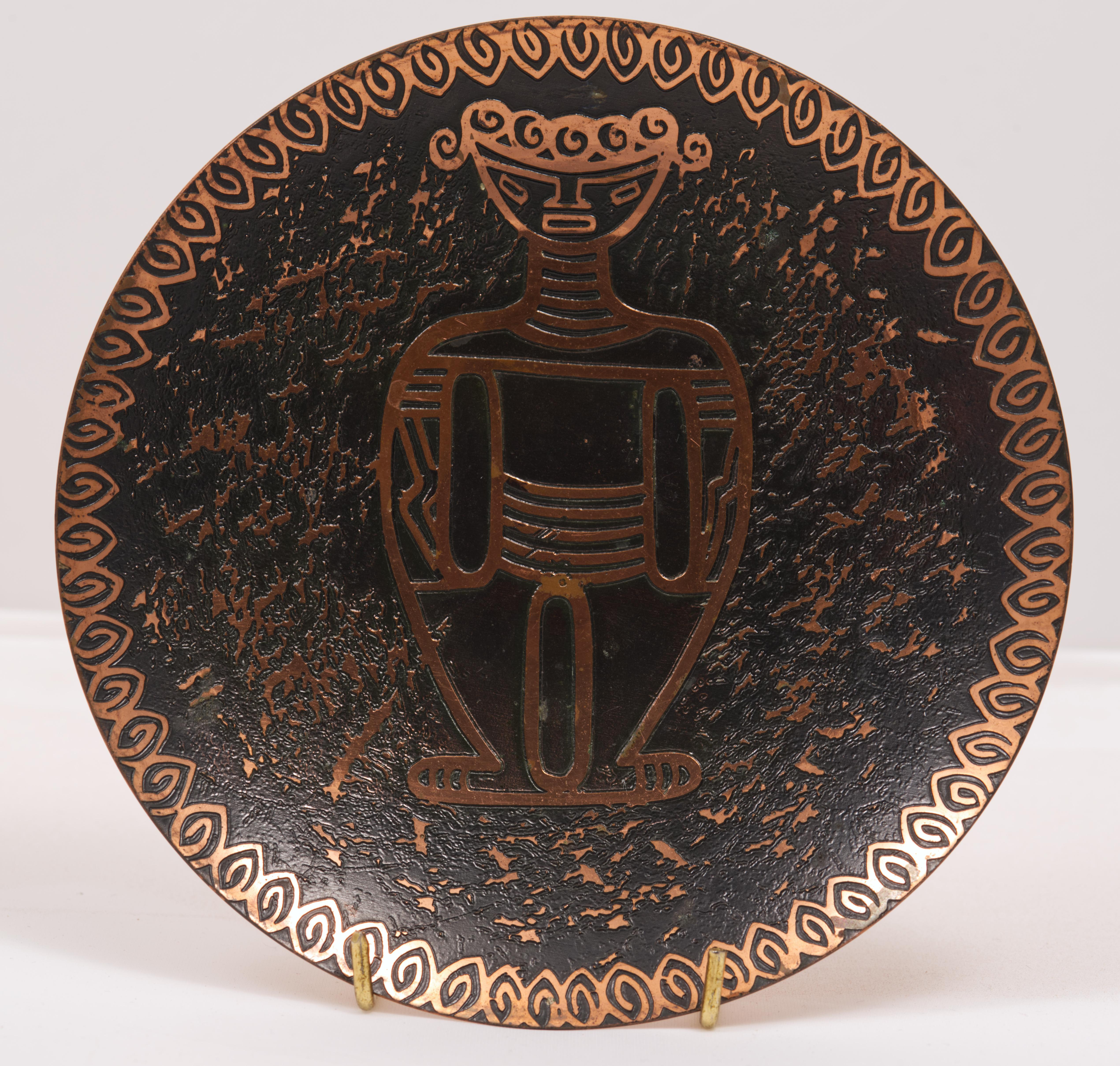 Raro e inusual plato o cuenco decorativo con un diseño modernista de una figura humana, rodeada de un fondo texturizado; el borde está adornado con una cenefa gráfica abstracta. La paleta mínima de colores latón y esmalte negro permite que la