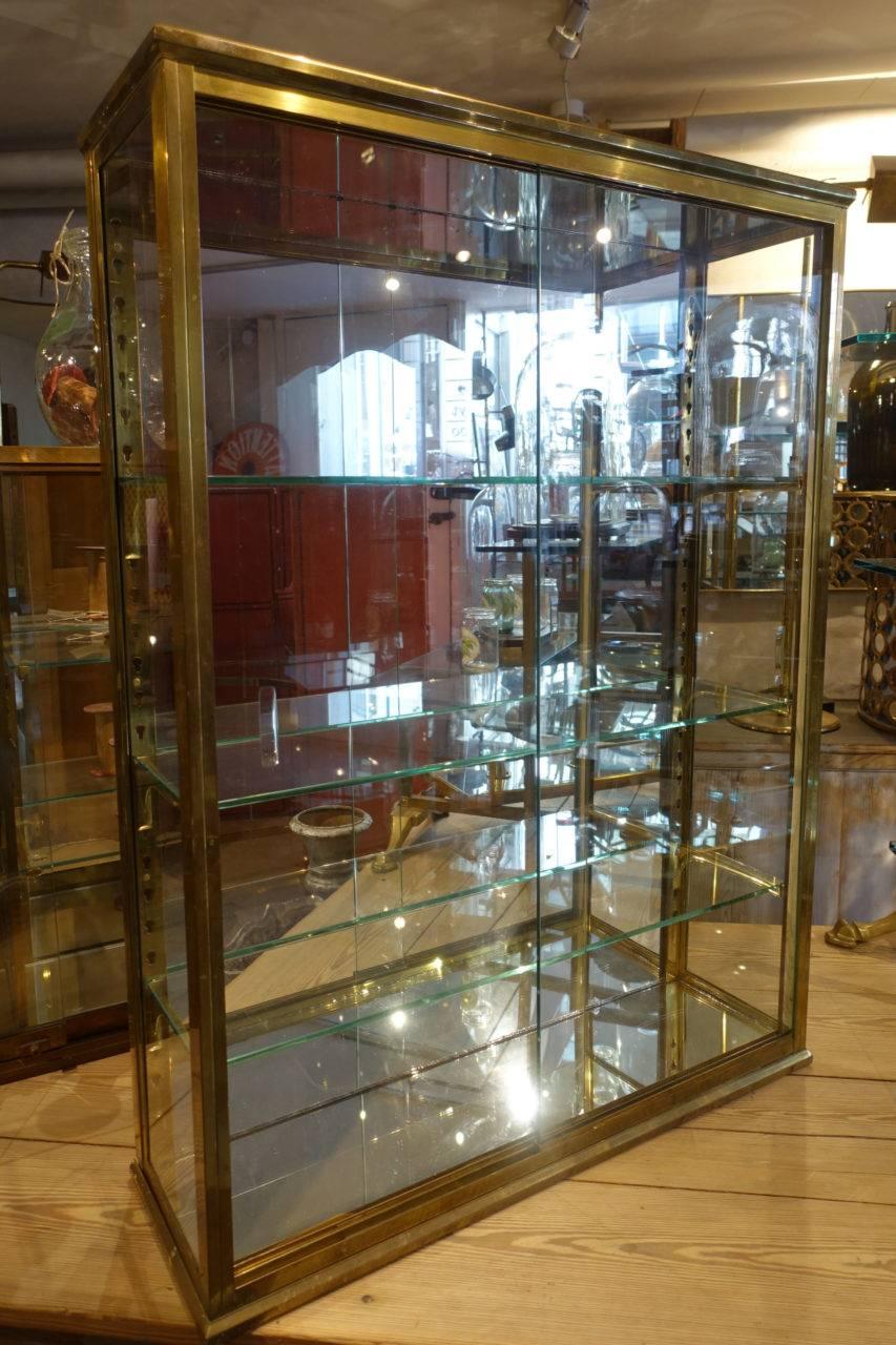 Elegant, tall and beautiful vintage French shop display cabinet, from the start of the 20th century. Brass frame and sliding glass doors and etched glass shelves. Mirrored back and floor panels. An especially quality and handsome unit, to display