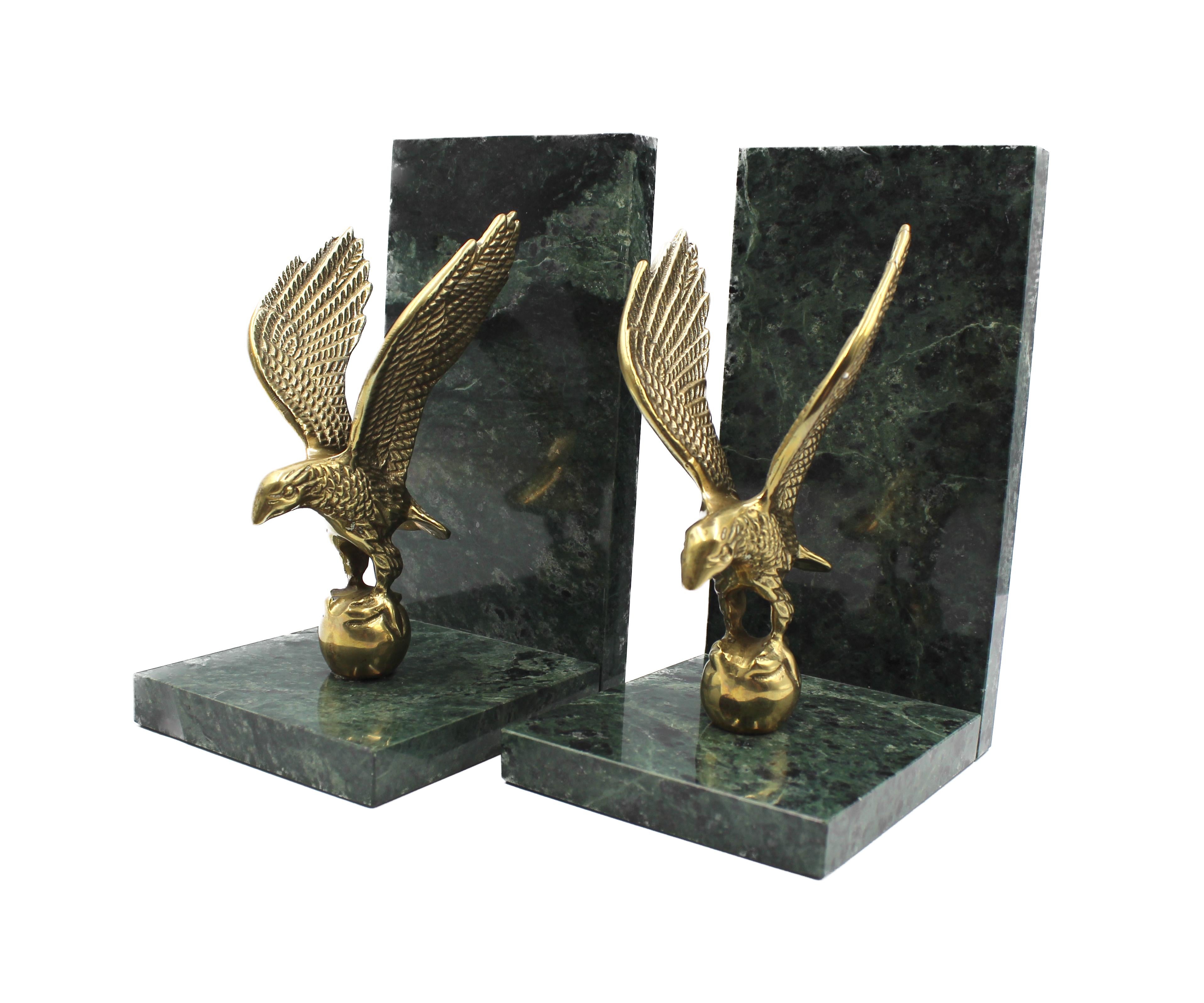 This is a vintage pair of eagle bookends, dating to the early 20th century. The bookends feature brass eagles affixed to green marble bases. The eagles appear to be in mid-flight, with widely spread and open wings that arch upwards. The eagles'