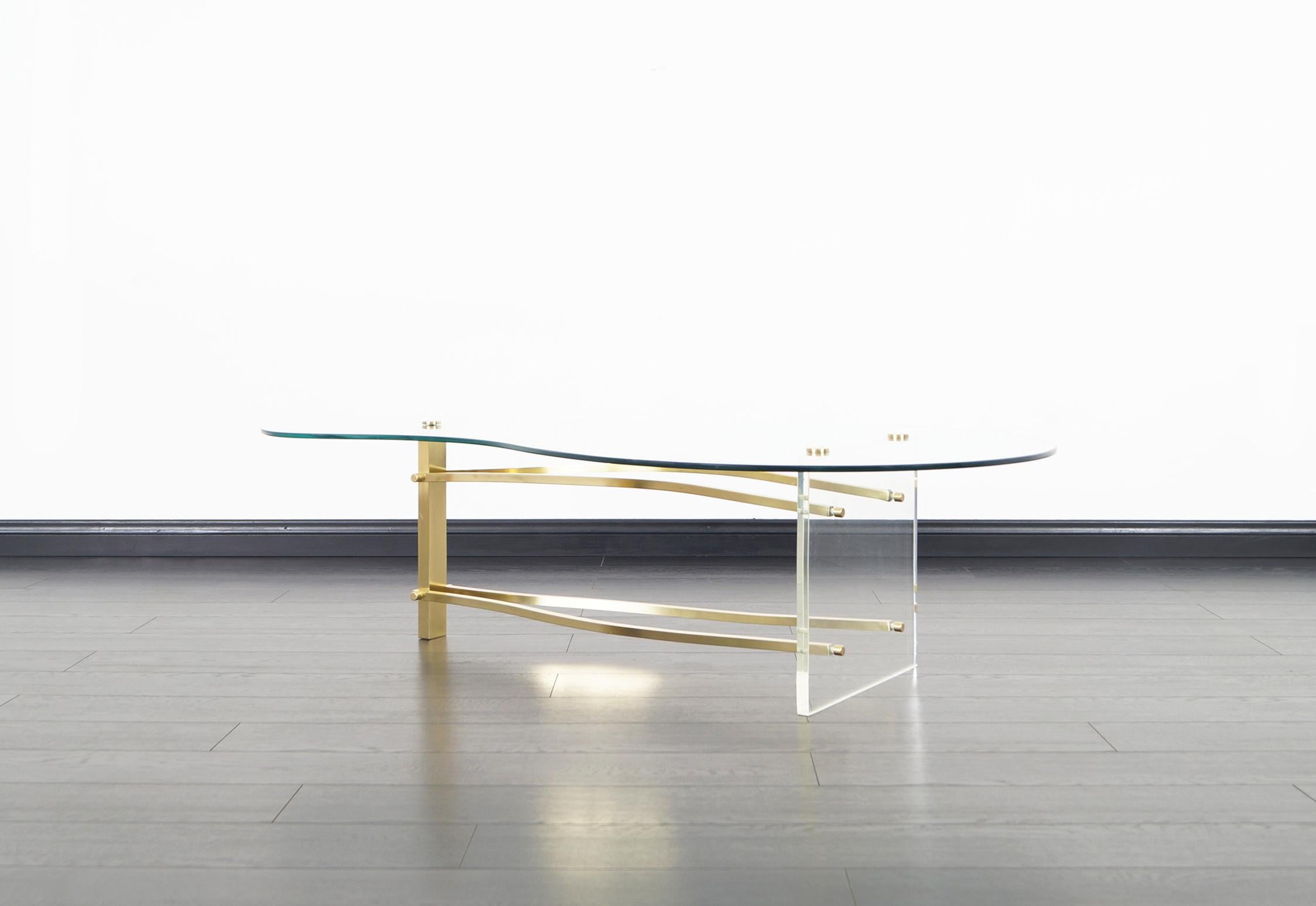 Vintage brass and Lucite coffee table in the manner of Charles Hollis Jones. Features a kidney shaped glass top that sits over a unique sculpted brass stretchers that's connecting to a square Lucite base and brass leg.