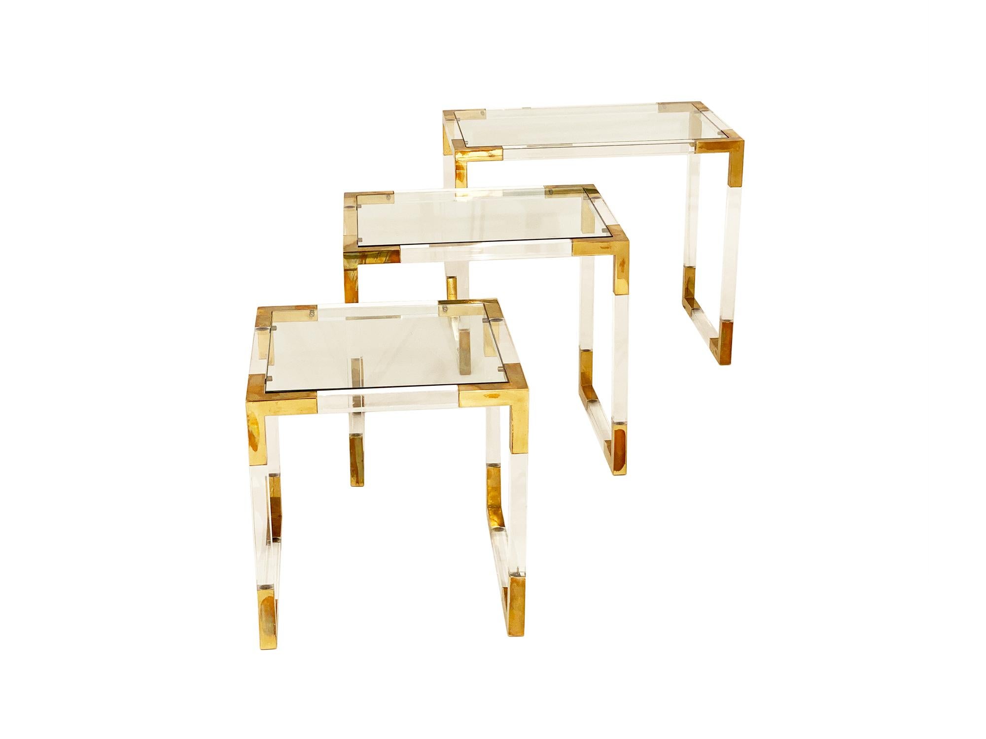 Brass and Lucite vintage nesting tables from France. Each table has a clear glass shelf and sits within the Lucite and brass structure. The measurements are for the largest table.