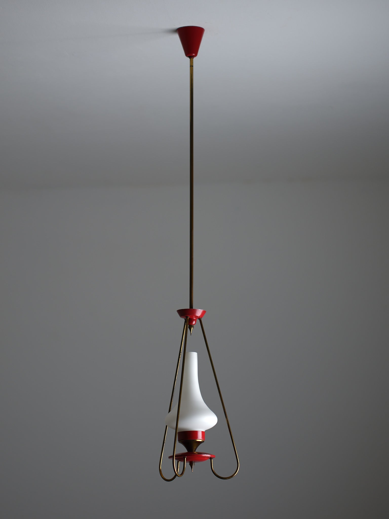 This pendant chandelier features a vintage design, crafted from brass with a naturally aged patina and a red lacquered metal body. The central light source is housed within an opaline glass shade, which diffuses light softly and evenly. Equipped