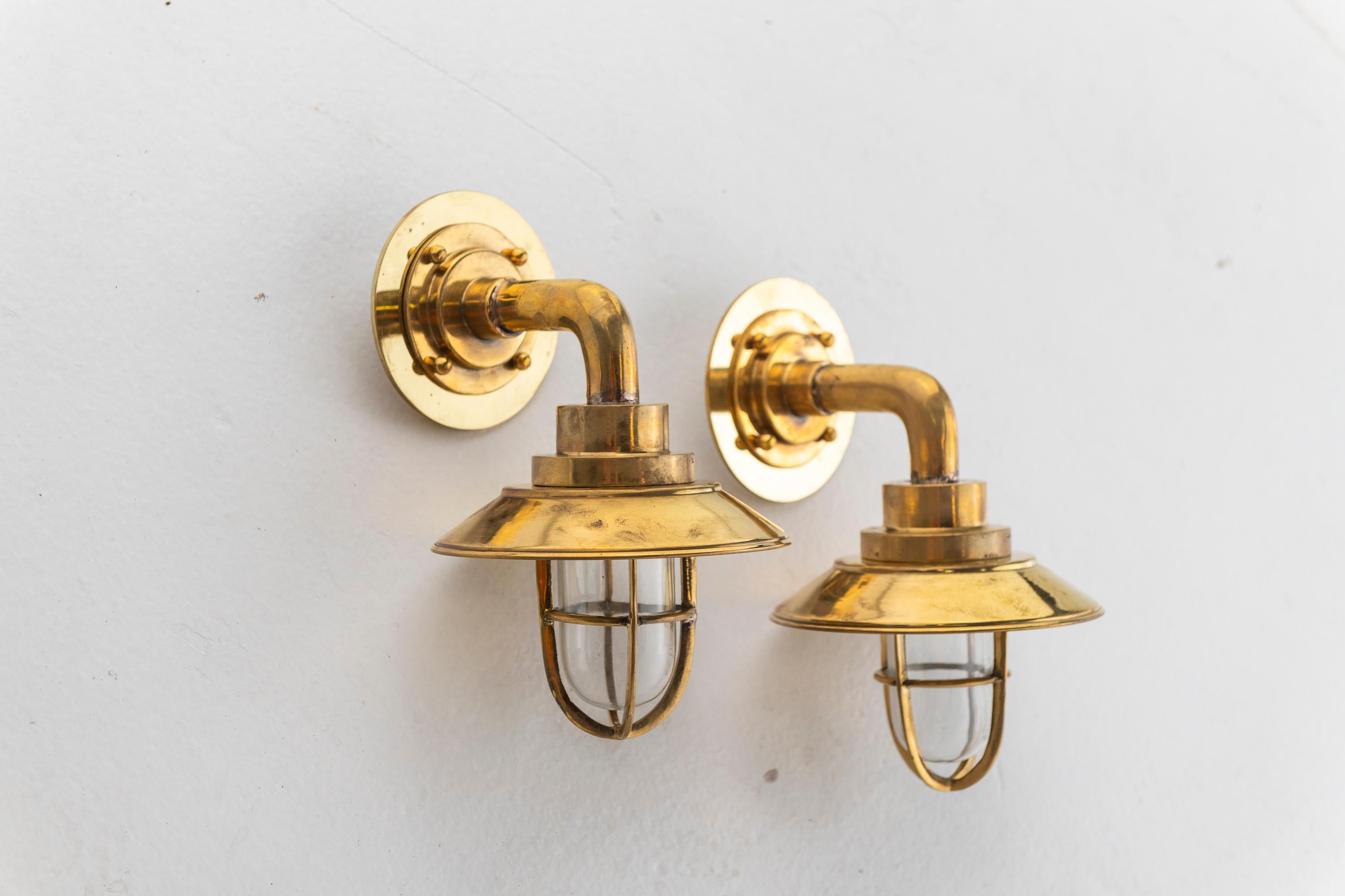 These Bent Shaped Ship Wall Sconces are made of solid brass and salvaged from a decommissioned ship. The sconce has a 90 degree bend, brass shade, vane top, and glass globe which are easily removed. The fixtures may be used both inside and outside.