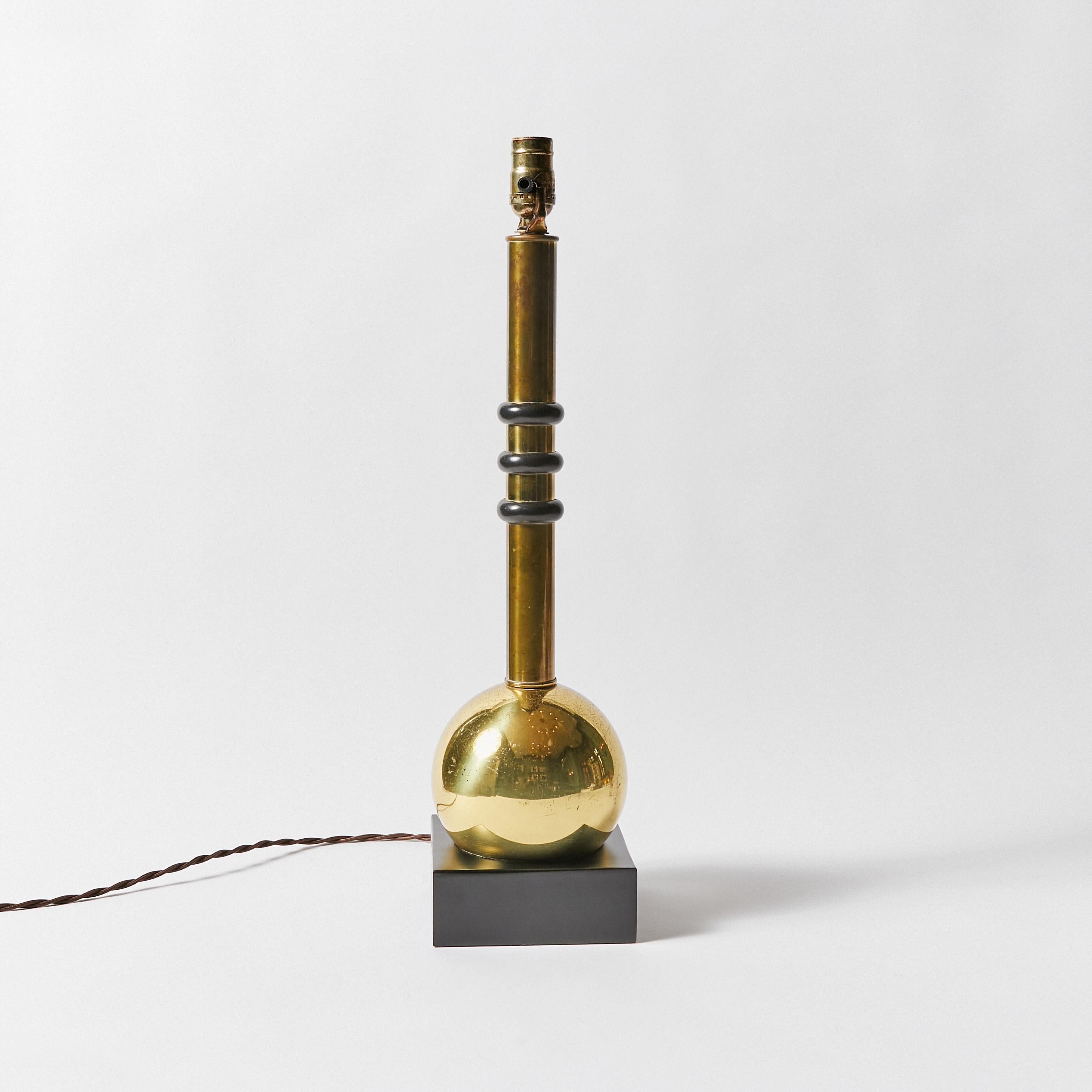 Lámpara de mesa vintage. Cuerpo de los matraces de latón con tres anillos de baquelita en el cuello. El cuerpo de la lámpara descansa sobre una base de madera.