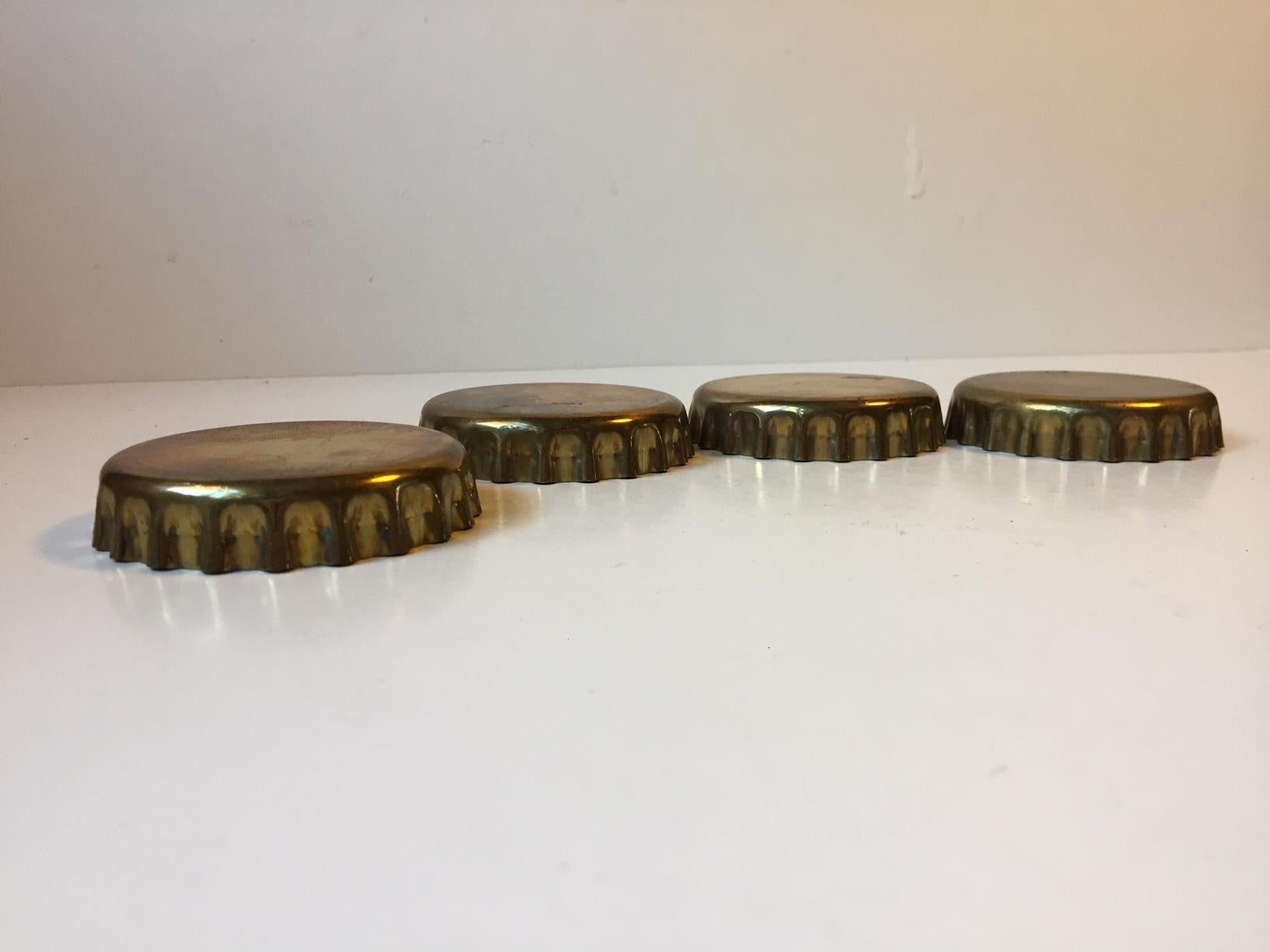 This is a set of 4 drink coasters in brass that are shaped as bottle caps. They are designed and manufactured by Georg Jensen in Denmark during the early 1980s.