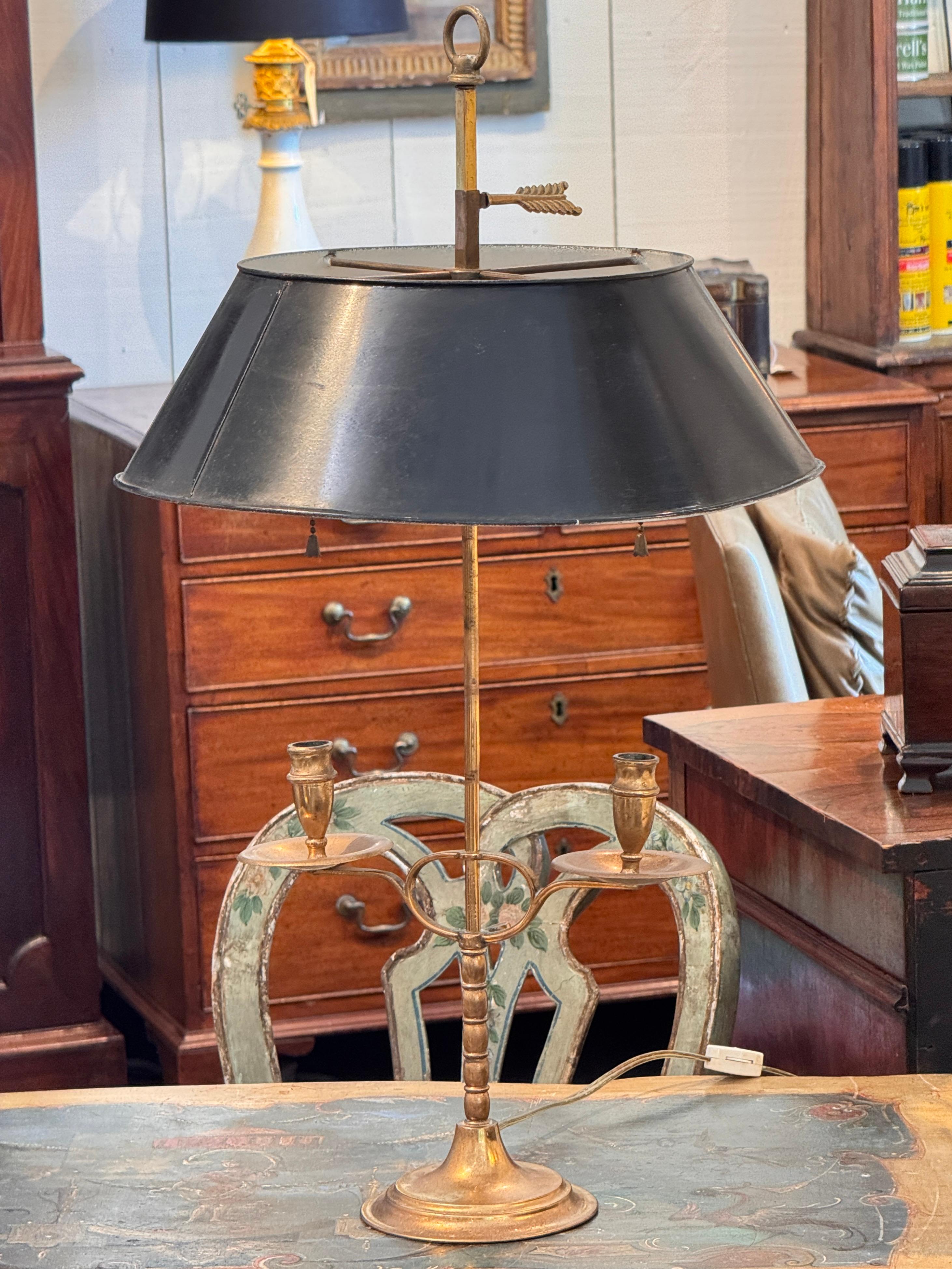 Lampada bouillotte d'epoca in ottone con design a due bracci con supporto centrale tornito e paralume originale in tole nero. Il paralume è regolabile su un'asta centrale, sormontata da un terminale ad anello e da un dettaglio a forma di freccia. La