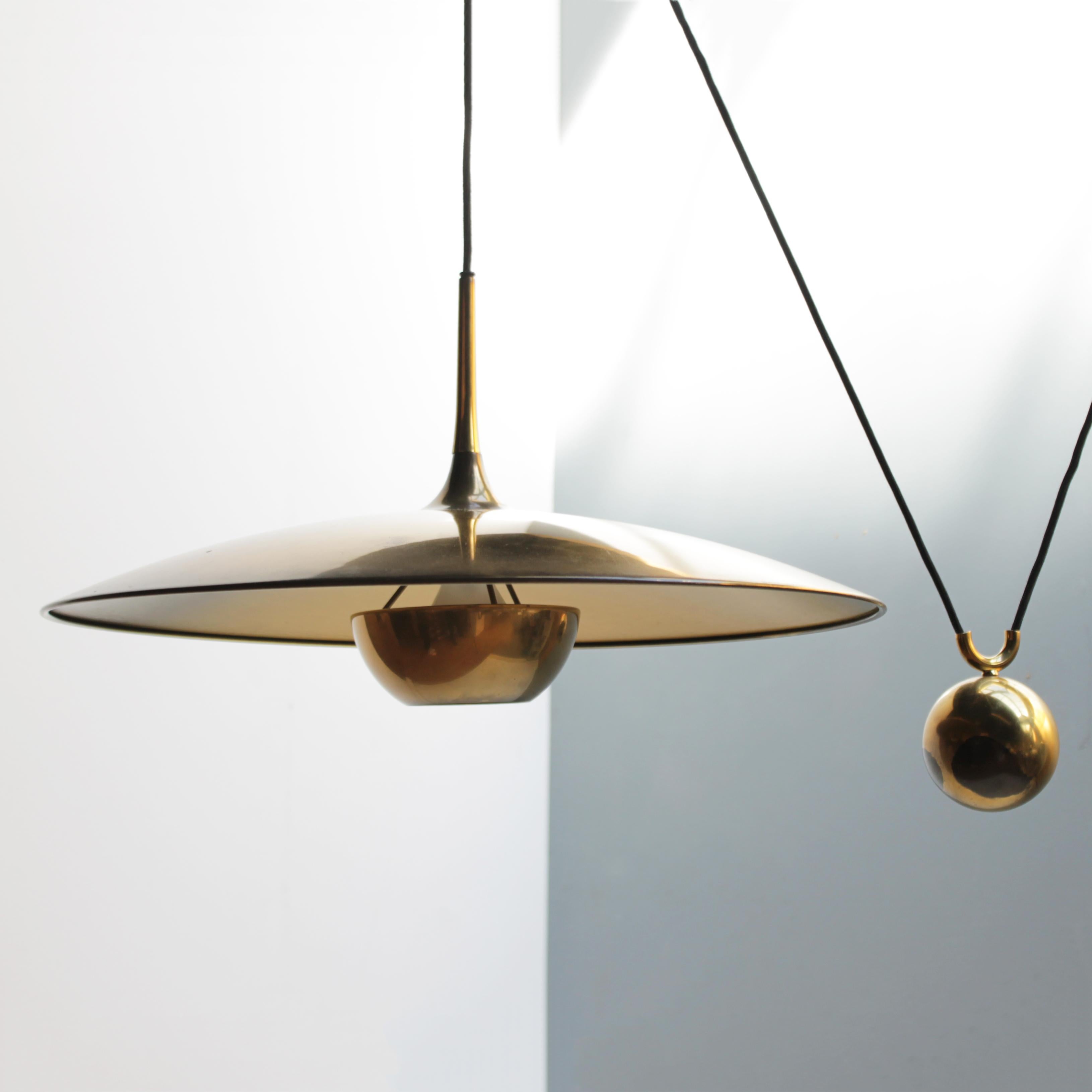 Original vintage modernist pendant, model Onos 55 in solid brass by Florian Schulz, circa 1975. 
The outer surface of the shade is in polished brass, while the inside has a brushed texture. With a brass reflector. This is the side counterweight