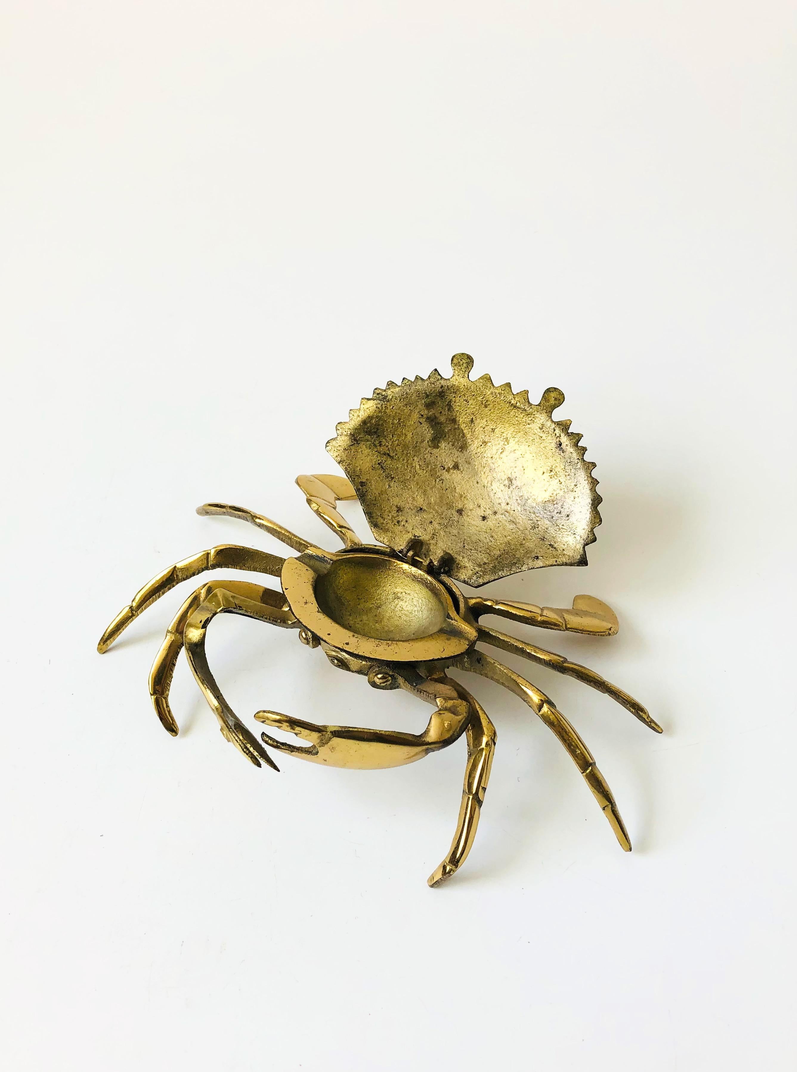 A vintage brass ashtray in the shape of a crab. The top hinges open to reveal an ashtray in the center. The ashtray can be removed so the crab could also be used as a box for storing small items. Beautiful detailing formed into the brass to create