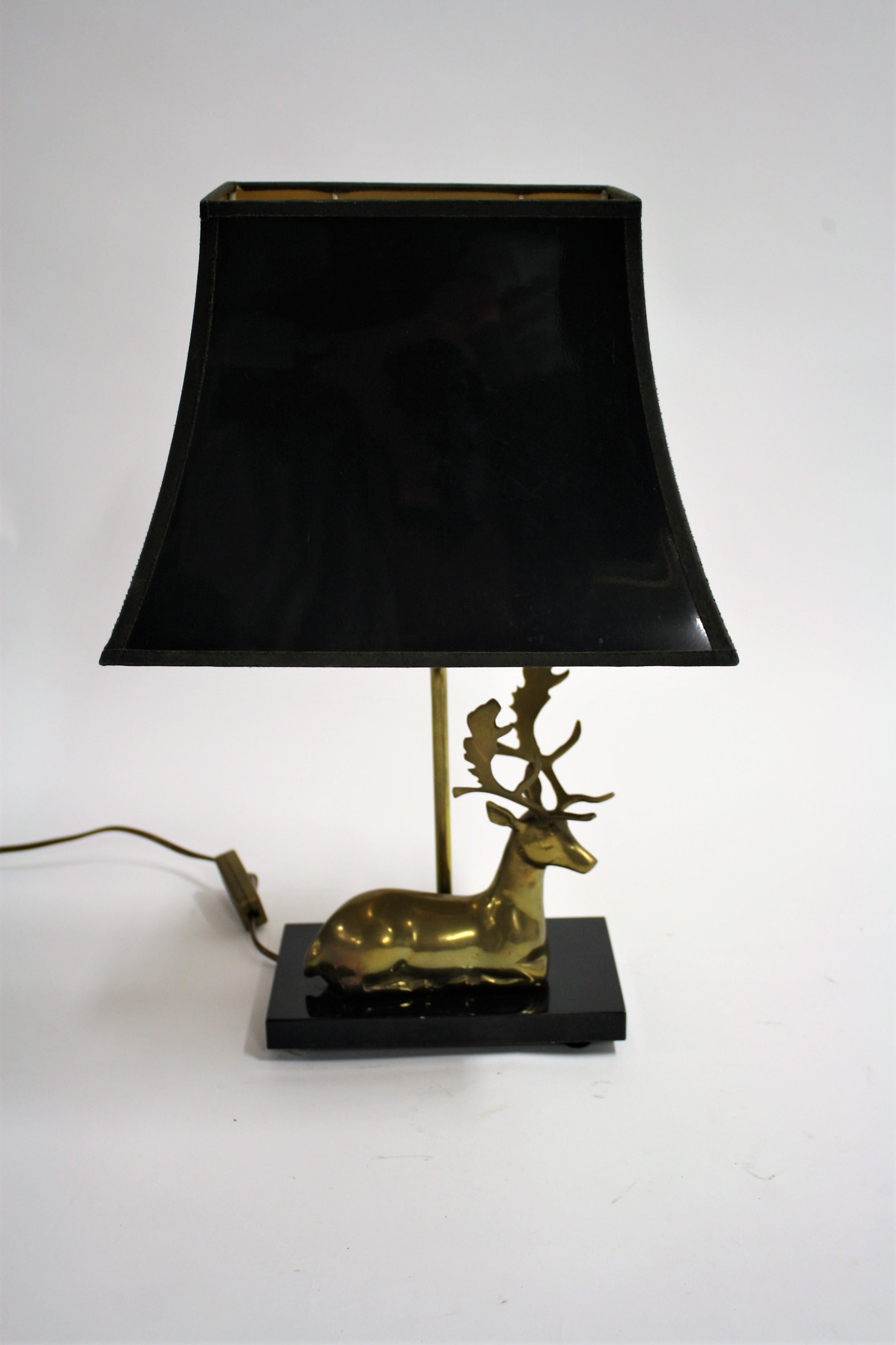 Hollywood Regency style table lamp featuring a patinated brass deer sculpture mounted on a black lacquered wooden base.

The lamp comes with the original lacquered and golden finished shade.

Tested and ready for use with a regular E26/E27 light