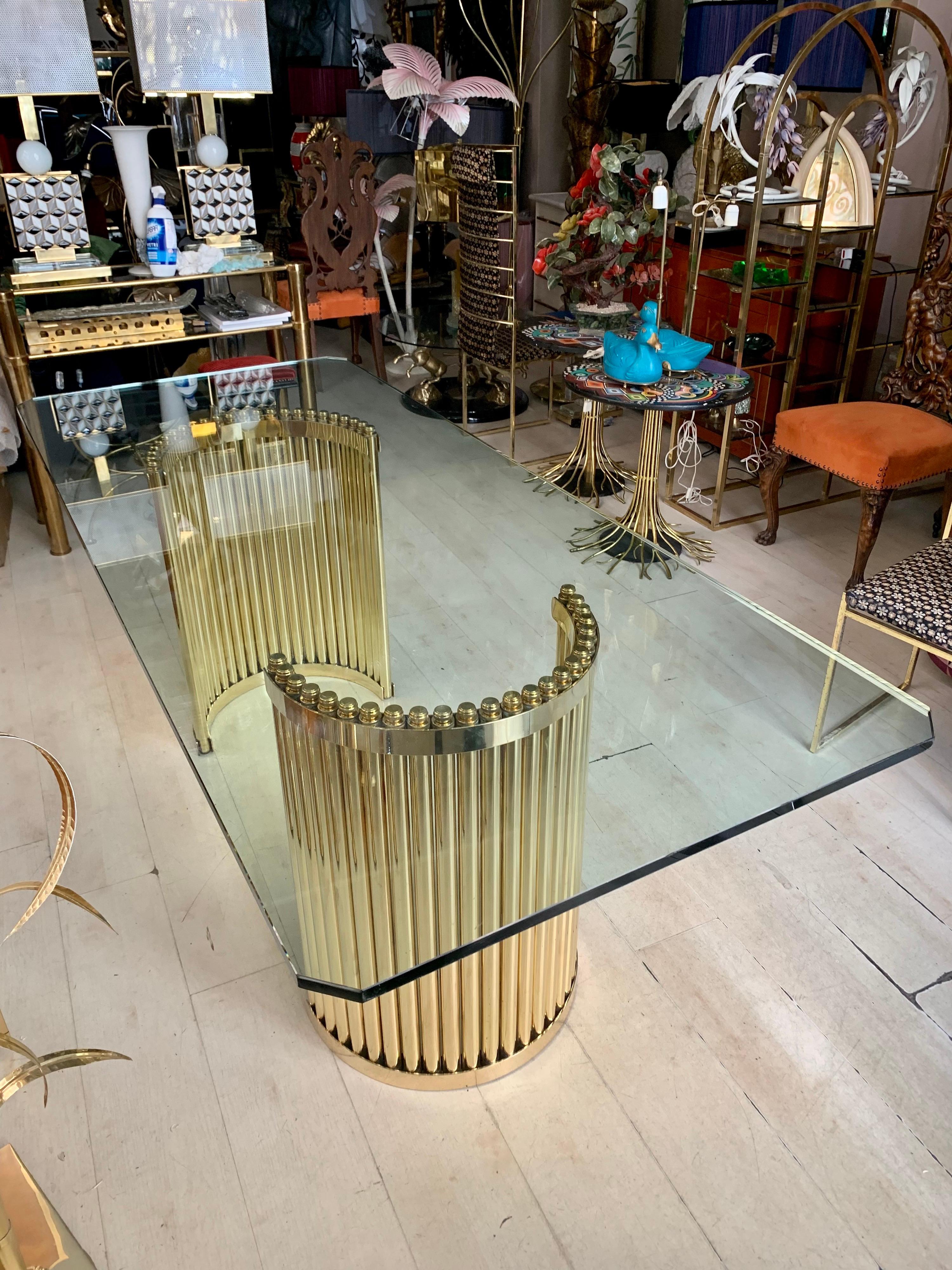 Vintage dining table with two brass semicircular supports and crystal top. The base is made of a multitude of brass tubes fixed in a single semicircular block. The tempered crystal top is thick mm 19 and it has a polished edge and squared corners.