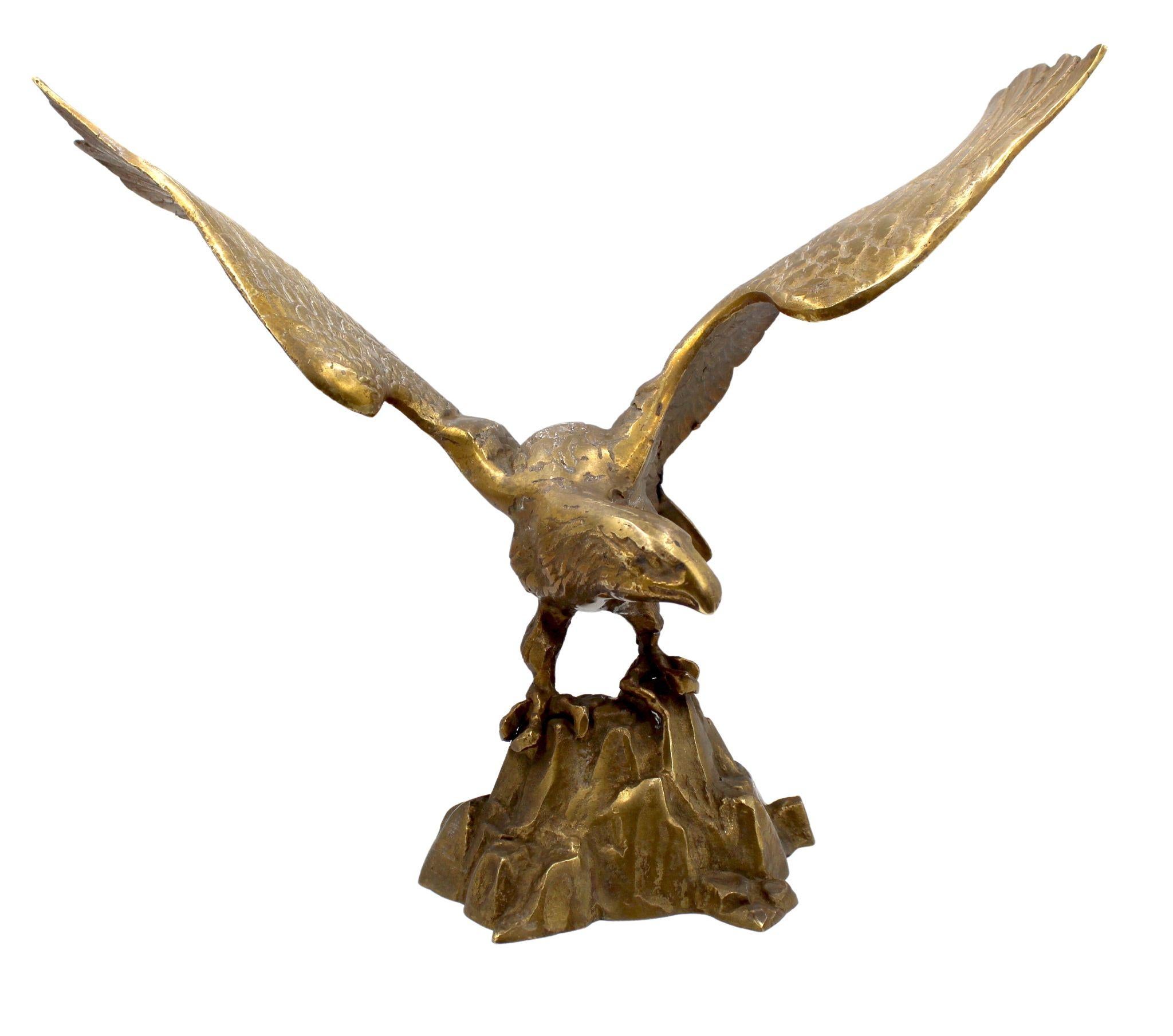 Presented is a vintage brass sculpture of a bald eagle on rocks. Made in America in the early 1960s, this sculpture features a large-scale, realistically cast bald eagle. The eagle has both of its wings spread wide for take-off, as his talons grip a