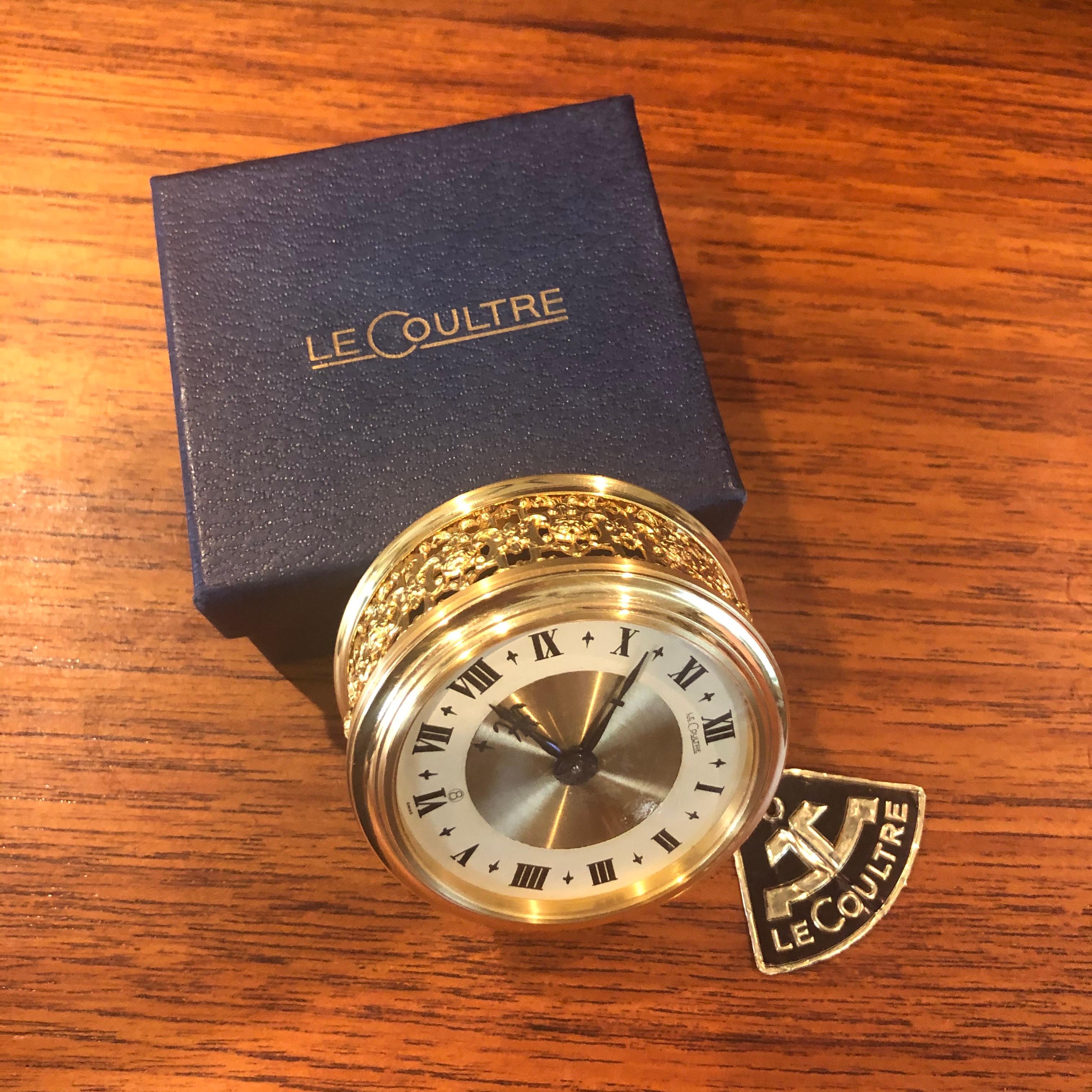 Lovely vintage brass eight day miniature travel alarm clock by LeCoultre, circa 1960s. The piece is essentially brand new in box with papers and warranty card and is model #77. Setup mode and dials on back.

The clock is Swiss made, beautiful
