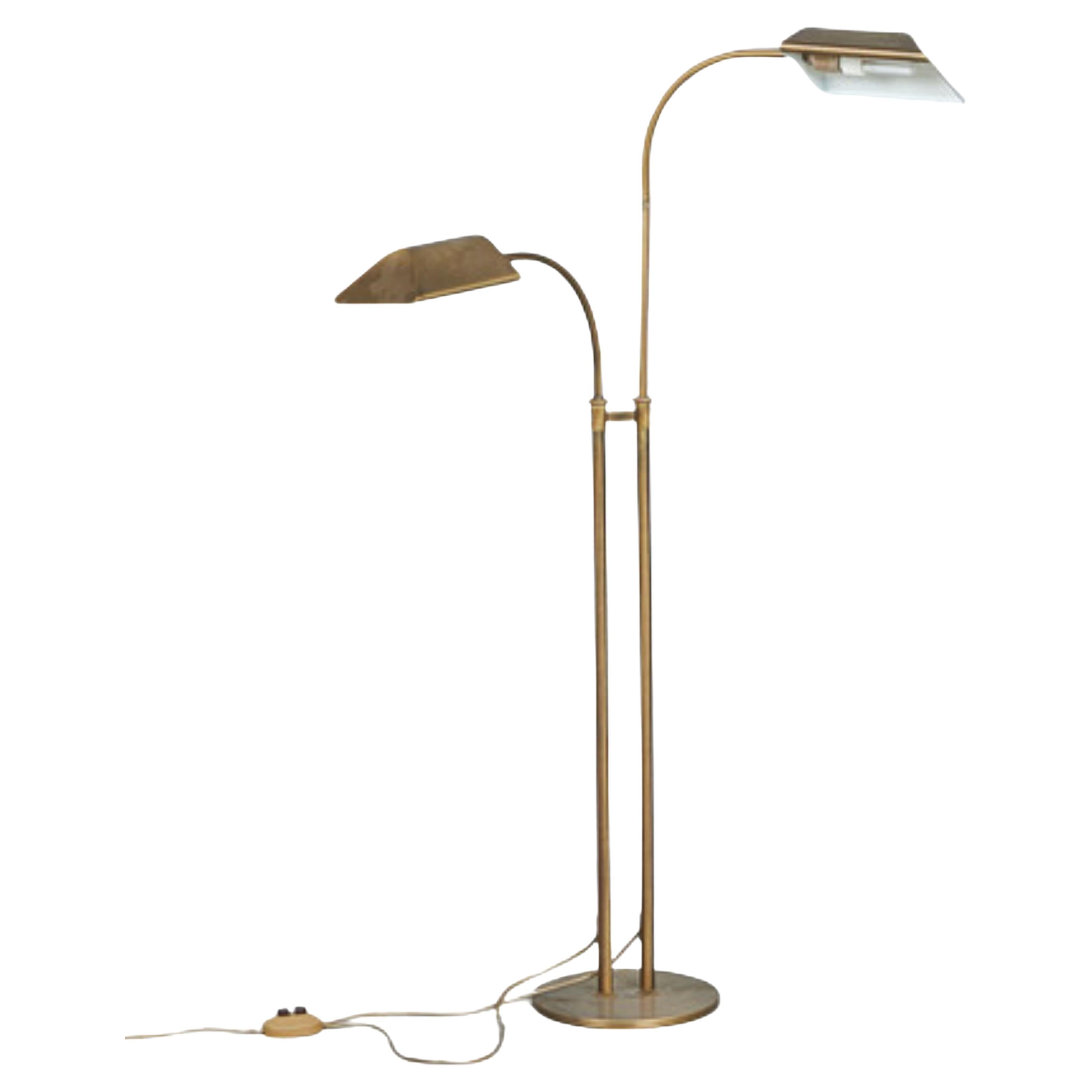 This 1970s floor lamp is an elegant and functional piece, crafted from brass with a sleek and modern design. It features two curved arms and a round base. The lamp also boasts two rectangular lamp heads that can be easily swiveled to direct the