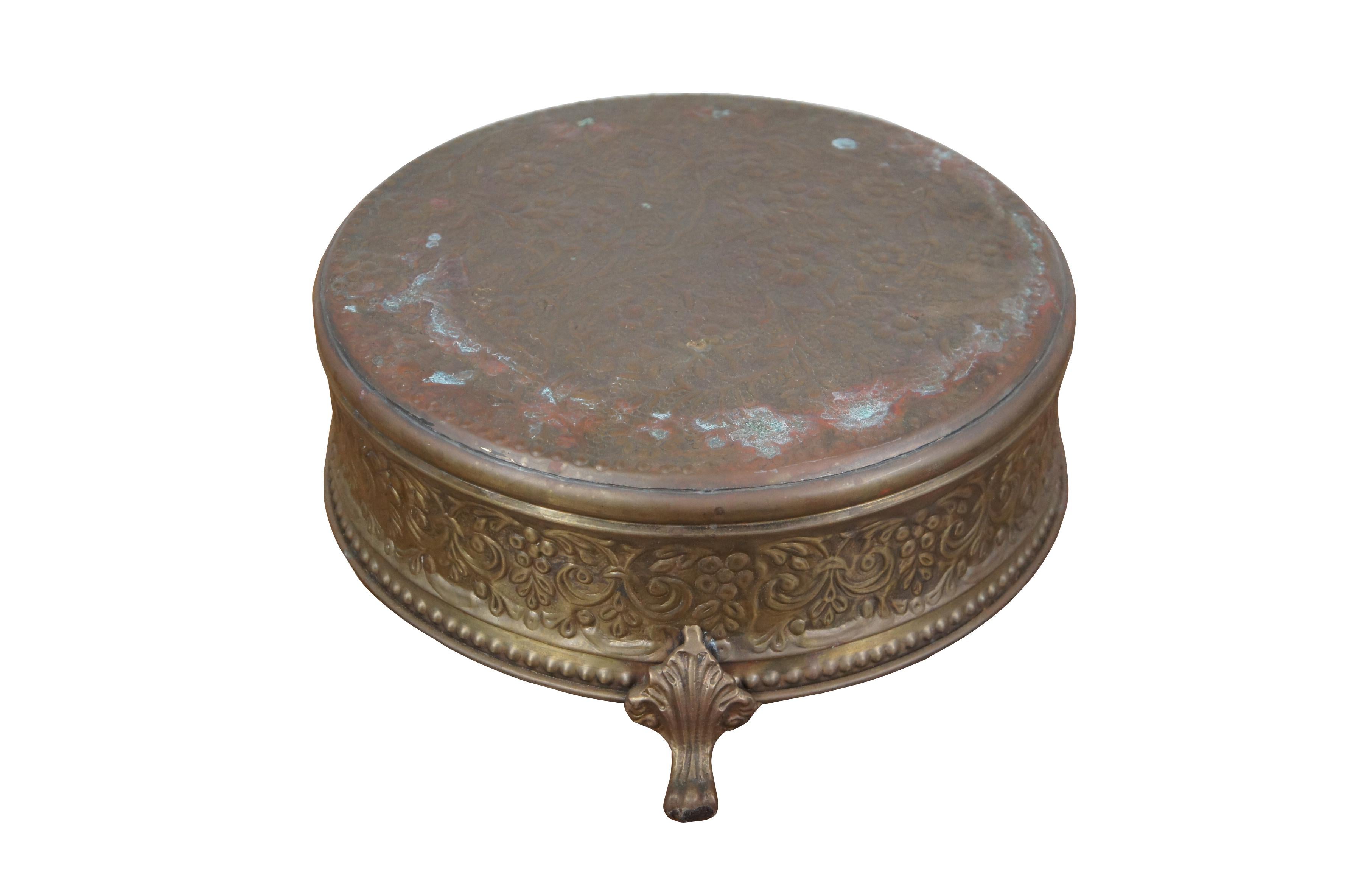 20th century round brass cake drum / cake stand / riser embossed with a floral and beaded design and footed base with scalloped paw feet.

Dimensions:
13
