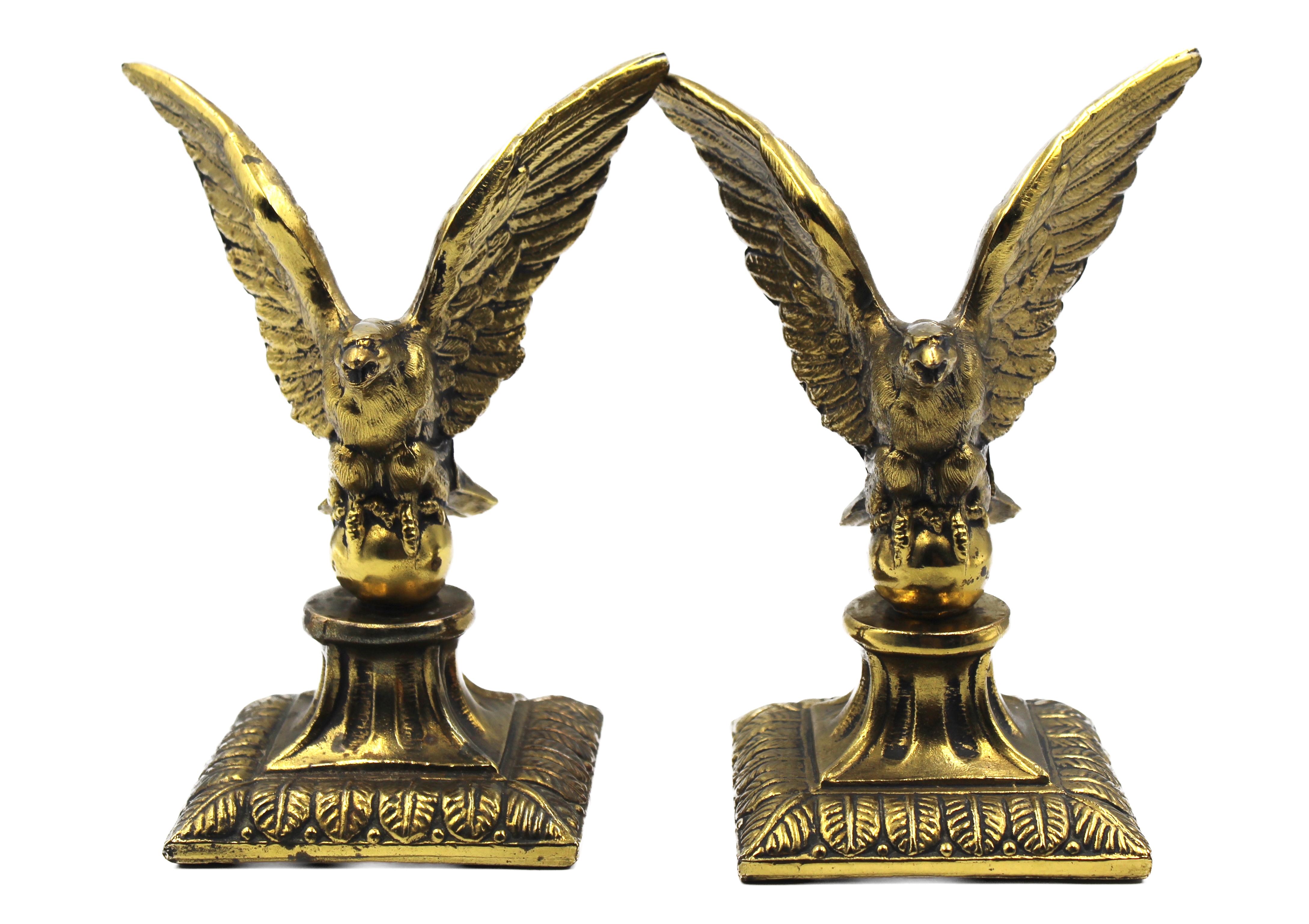 This is a vintage pair of eagle bookends, dating to the early 20th century. The bookends feature brass eagles surmounted on column bases. The eagles appear to be in mid-flight, with widely spread and open wings that arch upwards. The eagles' beaks