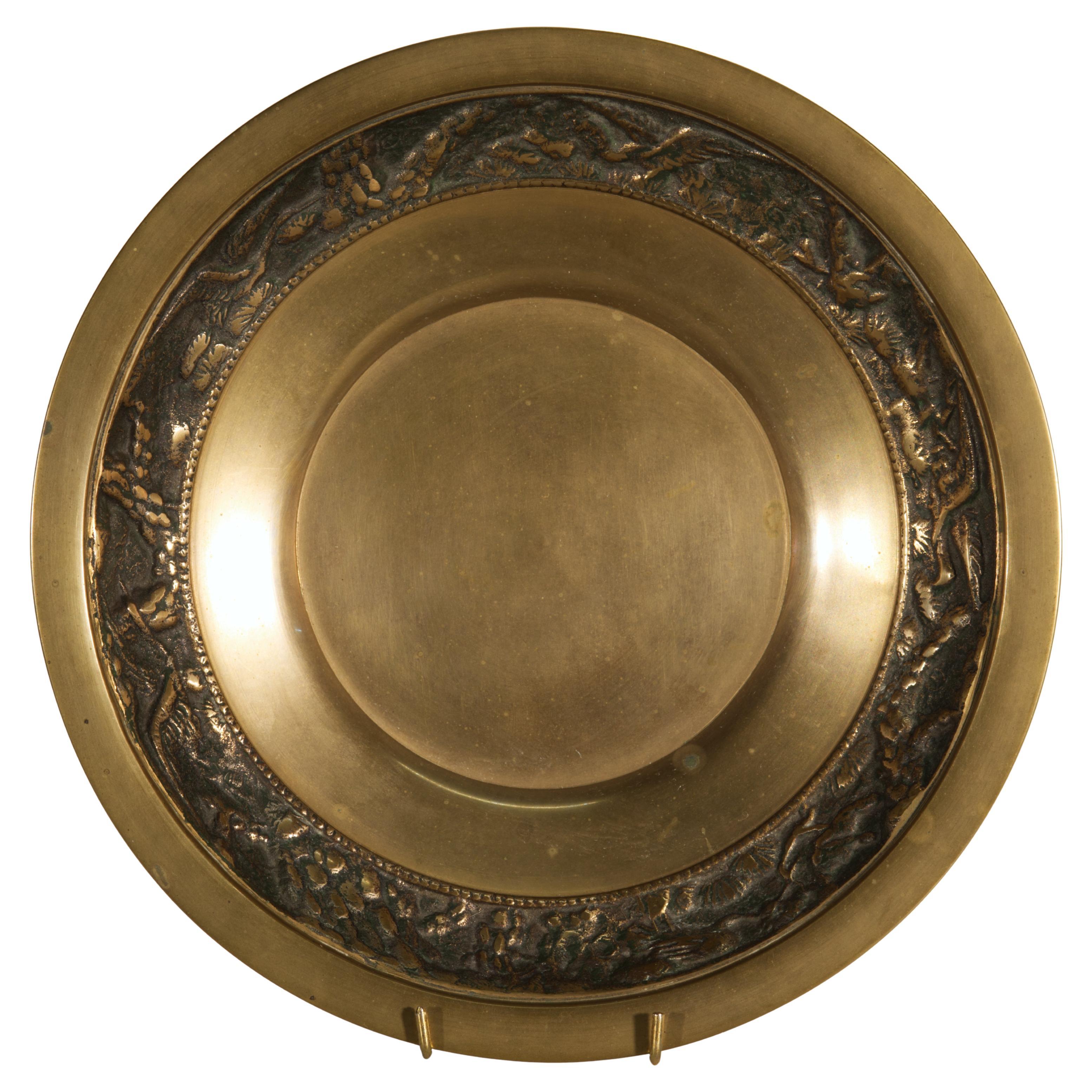 La coupe à pied en laiton vintage présente un large bandeau en relief très détaillé représentant des grues volant à travers des nuages et des branches d'arbre. La bande en relief est juxtaposée à un élément de bord plat minimaliste et à des surfaces