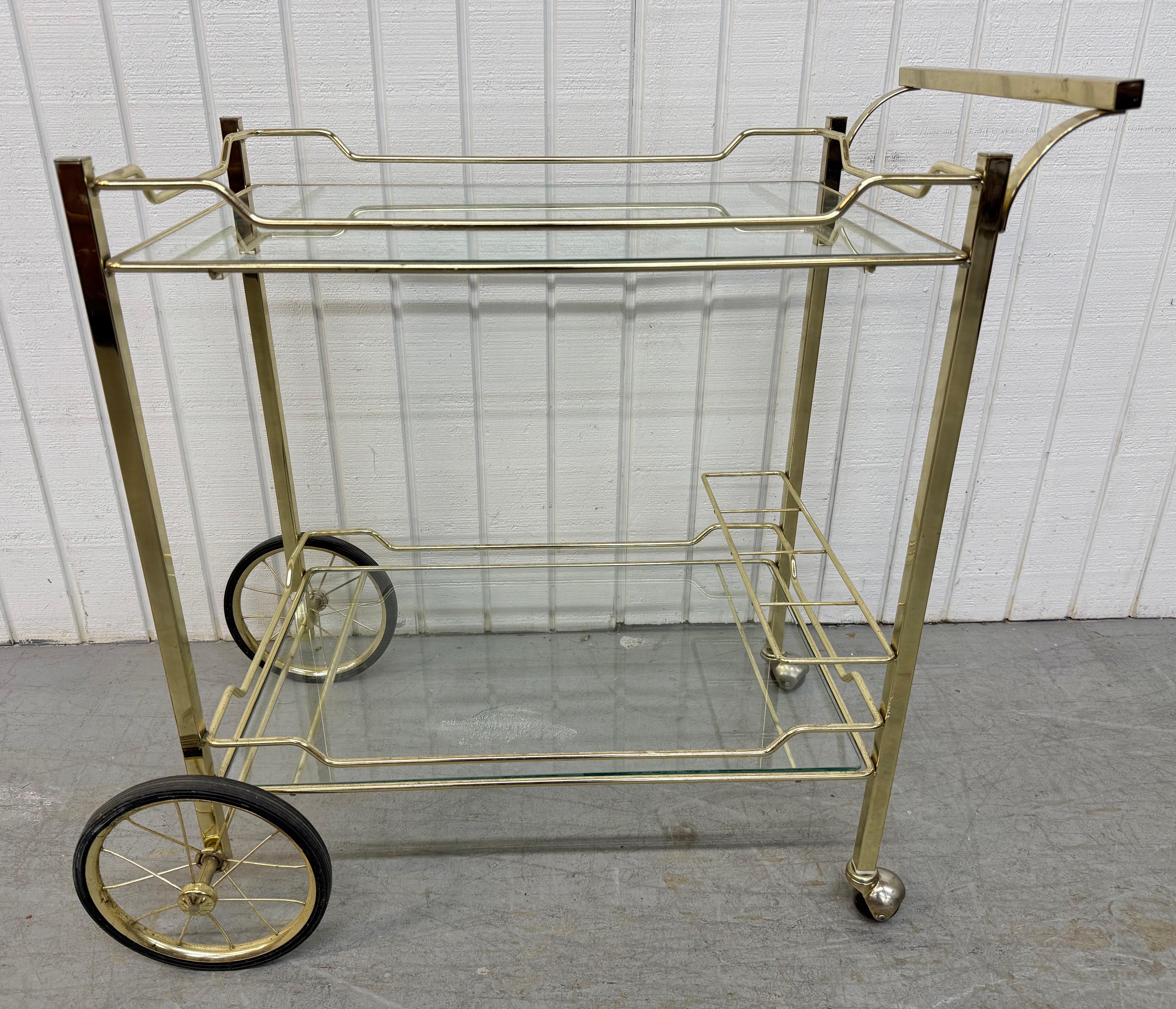 Cette annonce concerne un chariot de bar vintage. Avec un cadre en laiton, deux étagères en verre pour l'espace de stockage, une poignée pour se diriger, un porte-bouteille et des roulettes pour un transport facile. Il s'agit d'une combinaison