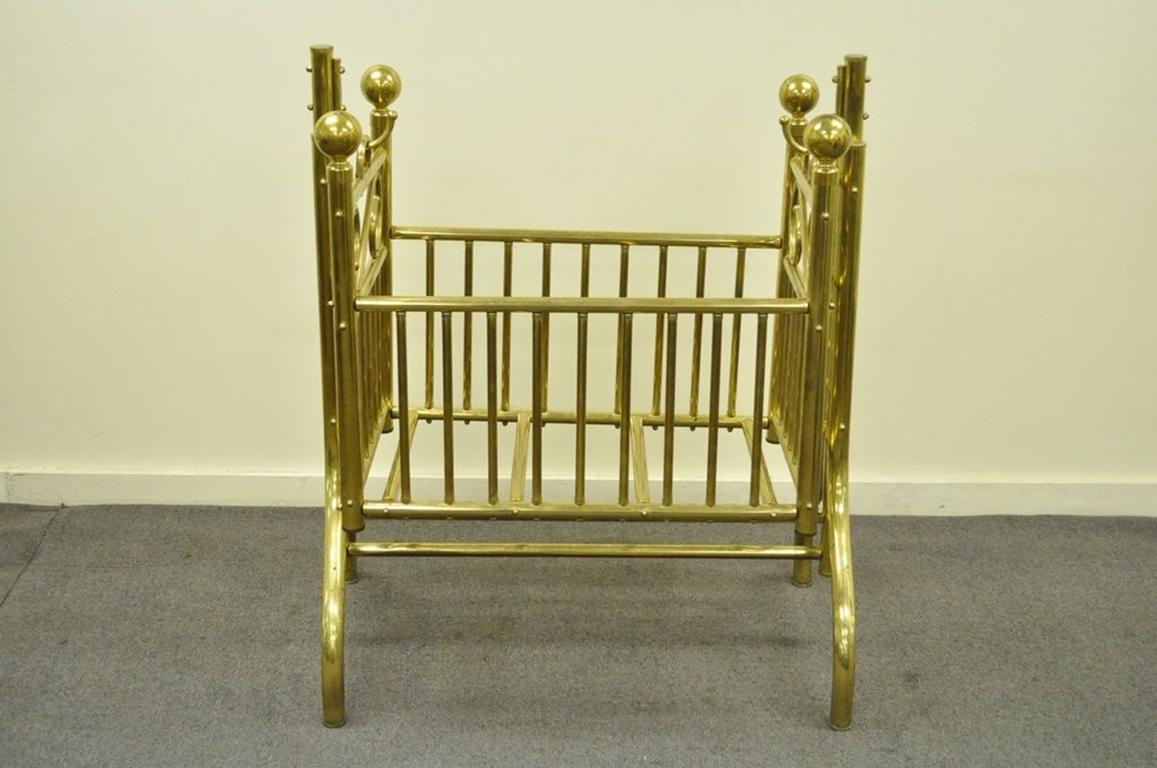 Striking vintage solid brass infant's suspended rocking cradle in the Victorian style. The piece has a nice wide silhouette, large orb finials, and scrolled accents. The maker is unconfirmed, though this piece is very similar to the 