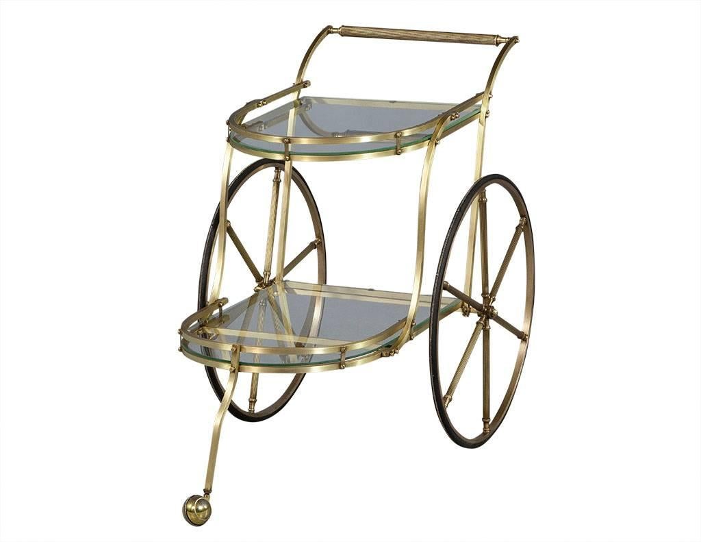 This Mid Century Modern tea trolley is purely whimsical.  Hailing from Italy, this serving cart has two large brass wheels with rubber tread and one large caster wheel at front.  The cart also has two half oval glass shelves, making it the perfect