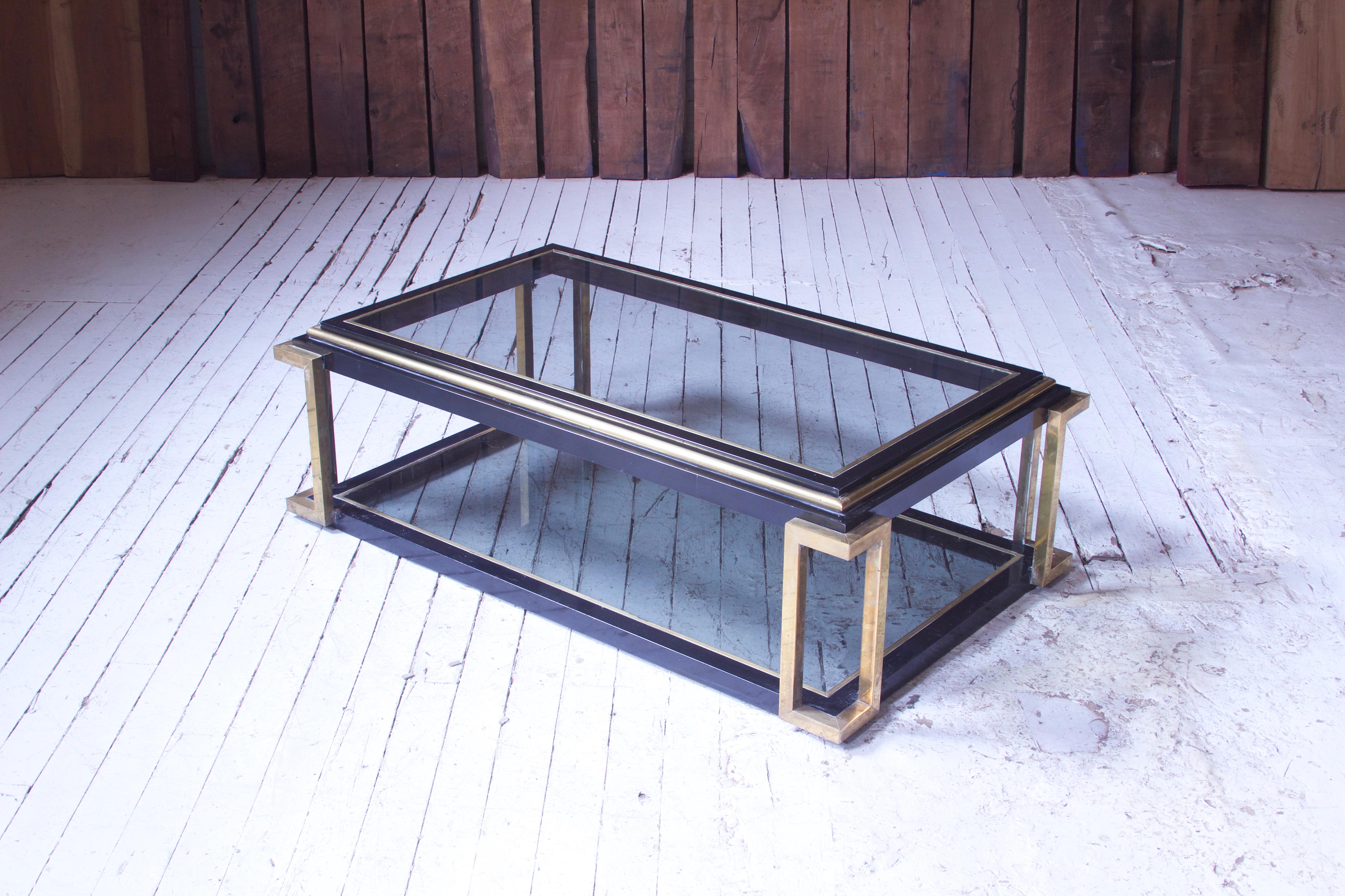 A lovely vintage two-tiered brass and lacquer coffee table with lightly-smoked glass in the style of Guy Lefevre for Maison Jansen, circa 1975. Interesting metalwork and rectilinear supports, an attractive and well-made piece.
